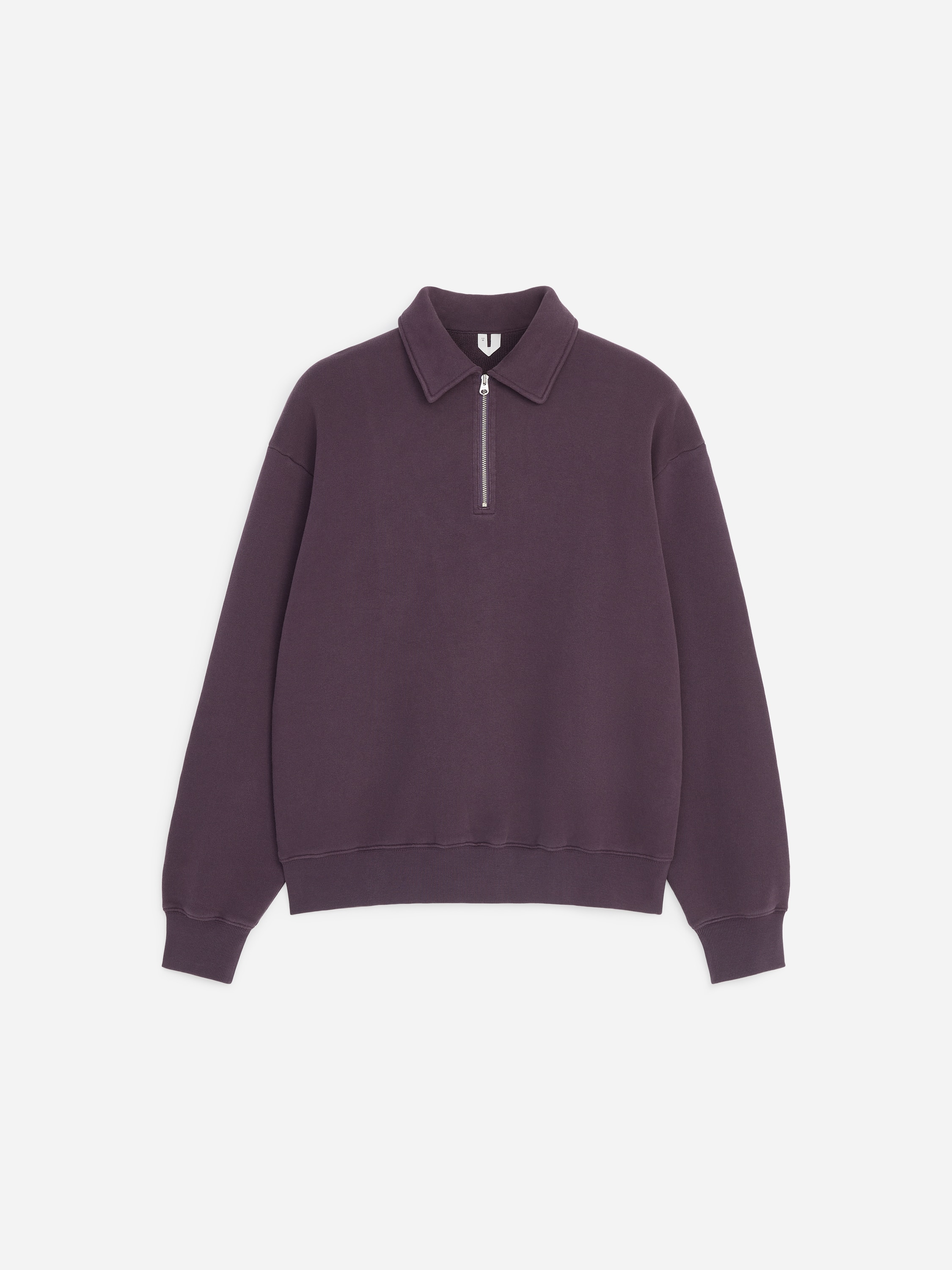 La modella indossa una felpa tinto capo di colore viola scuro, caratterizzata da colletto, chiusura frontale half-zip e bordi a coste. La felpa è indossata sopra una t-shirt bianca ed è abbinata a pantaloni scuri.