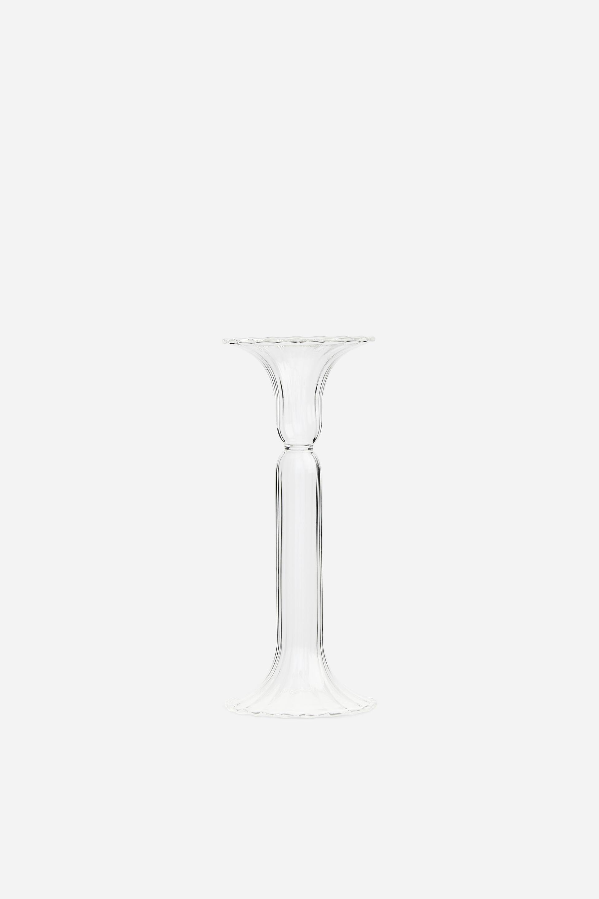 View larger image: A clear glass candlestick is standing upright, facing front, showcasing a ribbed, fluted design. It features a flared, wavy-edged top holder connected by a cylindrical stem to a matching flared, wavy-edged circular base.