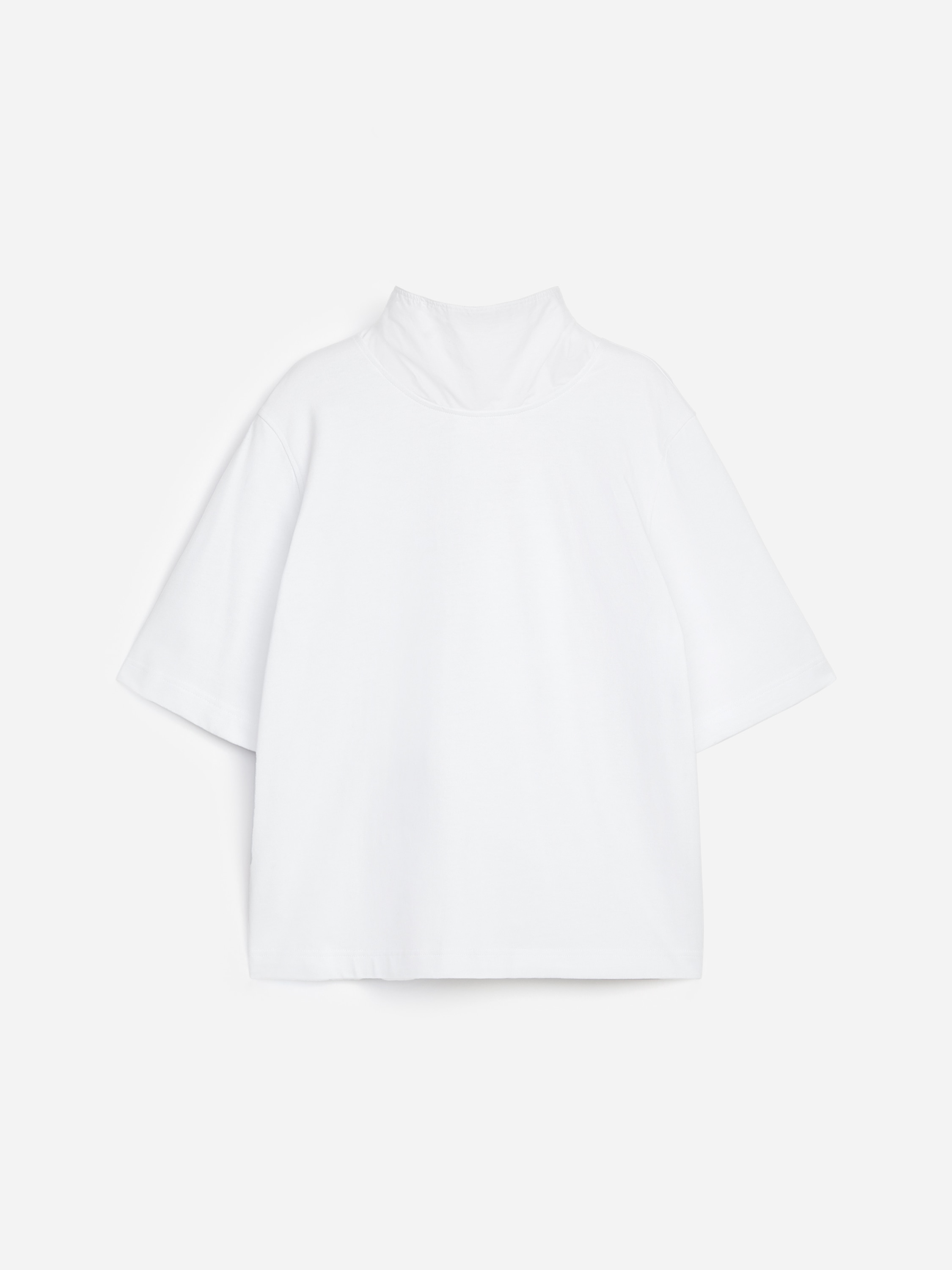A modelo estÃ¡ a usar uma camisola branca de corte regular, com gola subida, pormenor de echarpe drapeada e mangas atÃ© ao cotovelo. A camisola Ã© combinada com calÃ§as de ganga escuras e uma pulseira larga prateada.