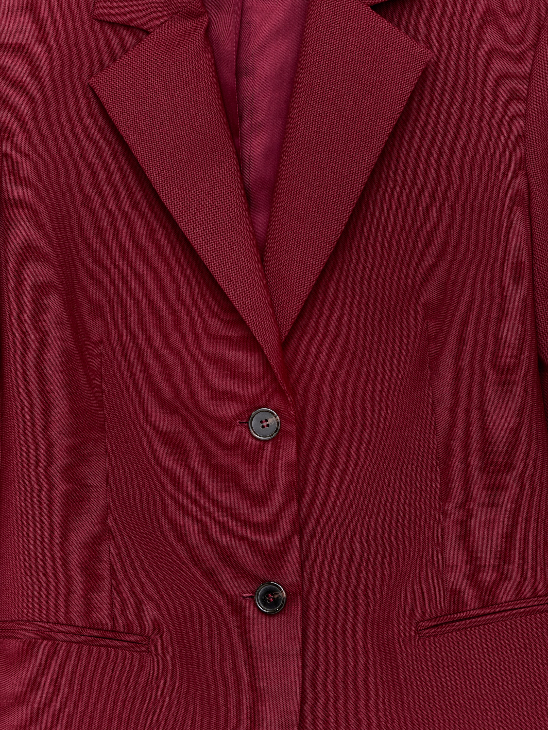 Visualizza immagine più grande: Un blazer monopetto realizzato in lana hopsack di un colore rosso intenso è presentato frontalmente. Presenta ampi revers a lancia, due bottoni rotondi scuri che chiudono la parte anteriore e una tasca a doppio filetto orizzontale sul lato inferiore sinistro.
