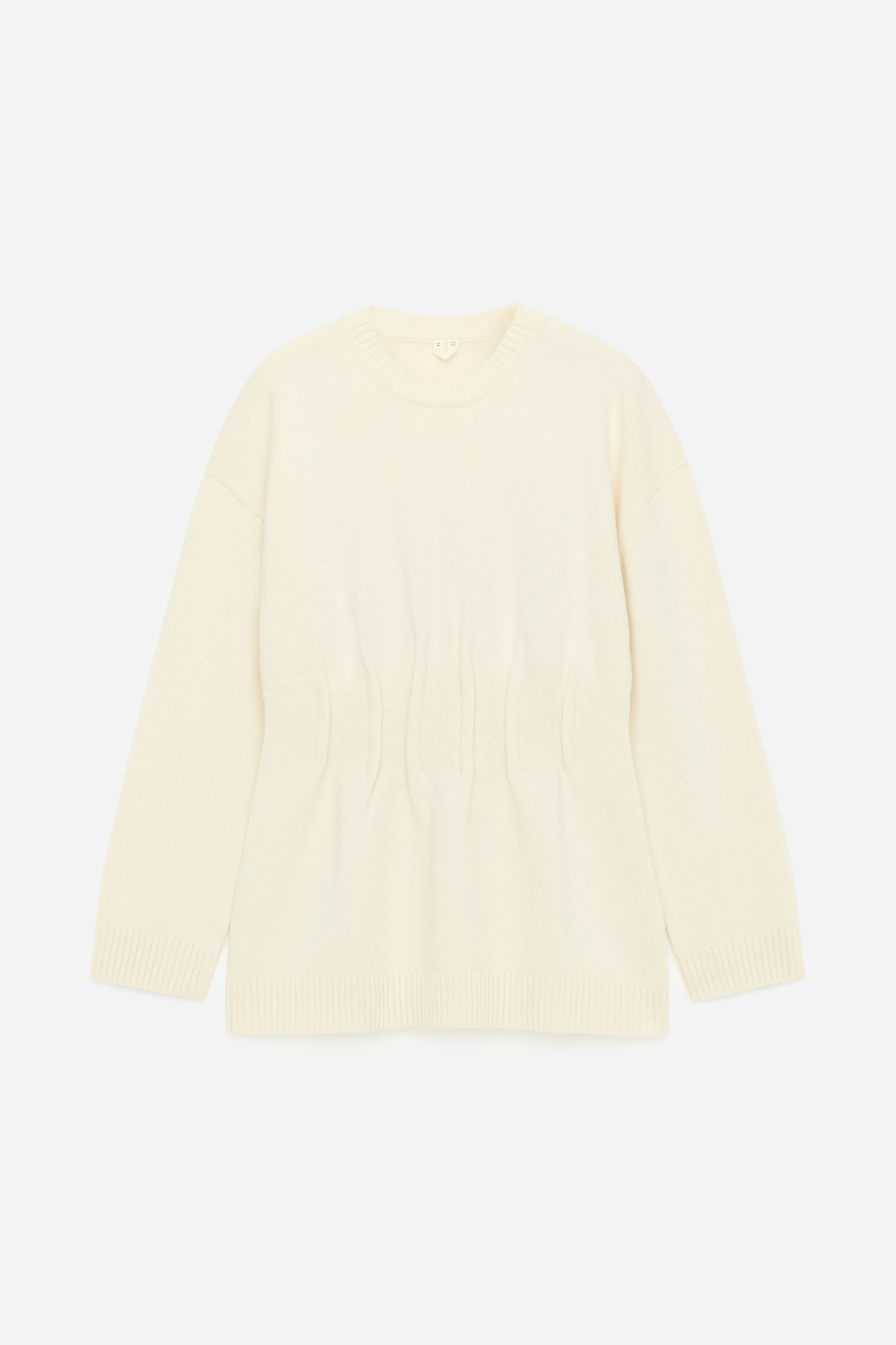 Grösseres Bild ansehen: Ein cremefarbener Pullover präsentiert sich in der Vorderansicht, mit einem gerippten Rundhalsausschnitt, langen Ärmeln mit gerippten Bündchen und einem gerippten Saum. Der vordere Rumpf zeigt ein gerafftes Design, das subtile vertikale Falten über der Taille erzeugt.