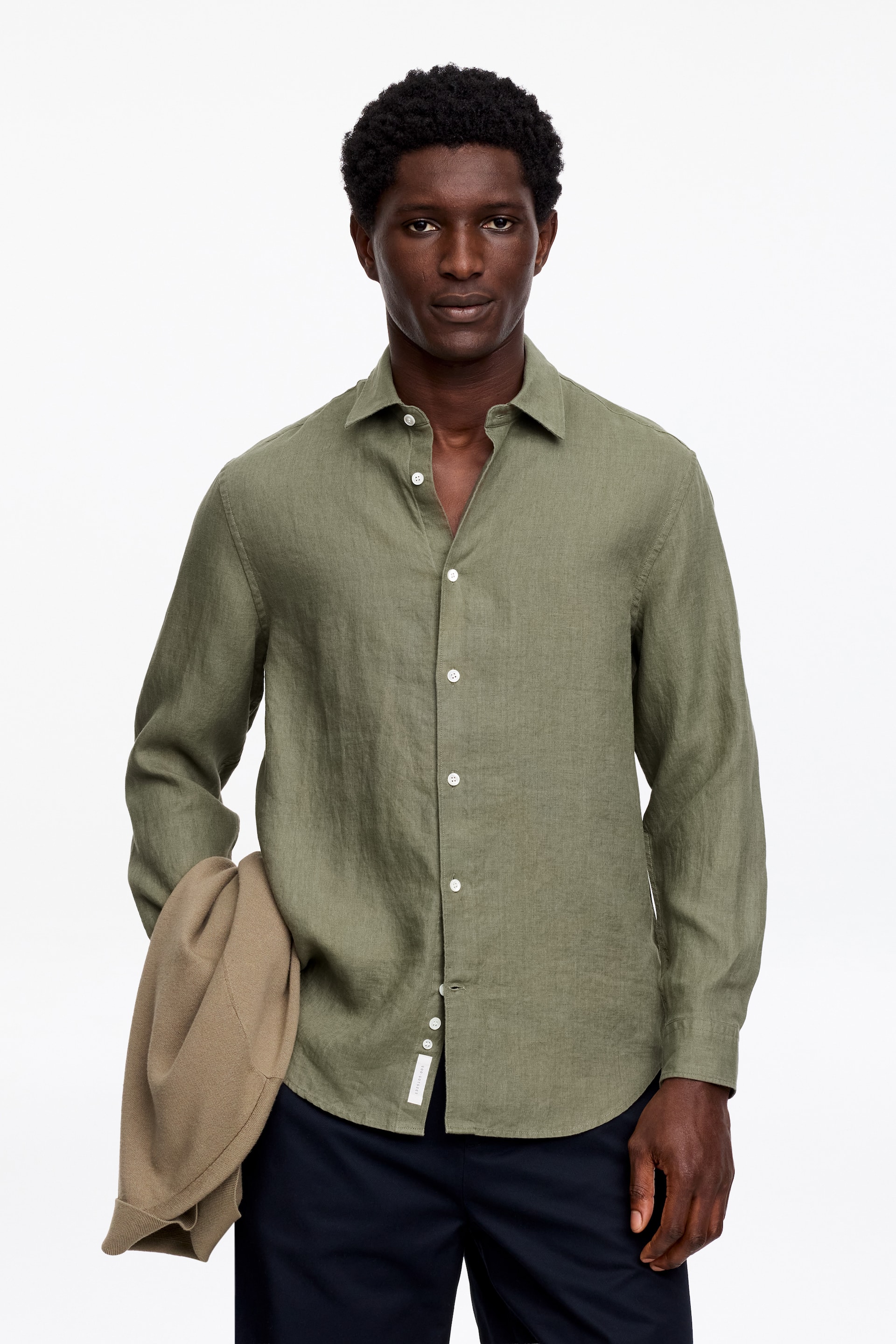 Grotere afbeelding bekijken: Een olijfgroen linnen overhemd met lange mouwen is naar voren gericht, met een spread kraag en witte knopen aan de voorkant. De bovenste knopen zijn losgemaakt, en het overhemd heeft een gebogen zoom en knoopmanchetten.