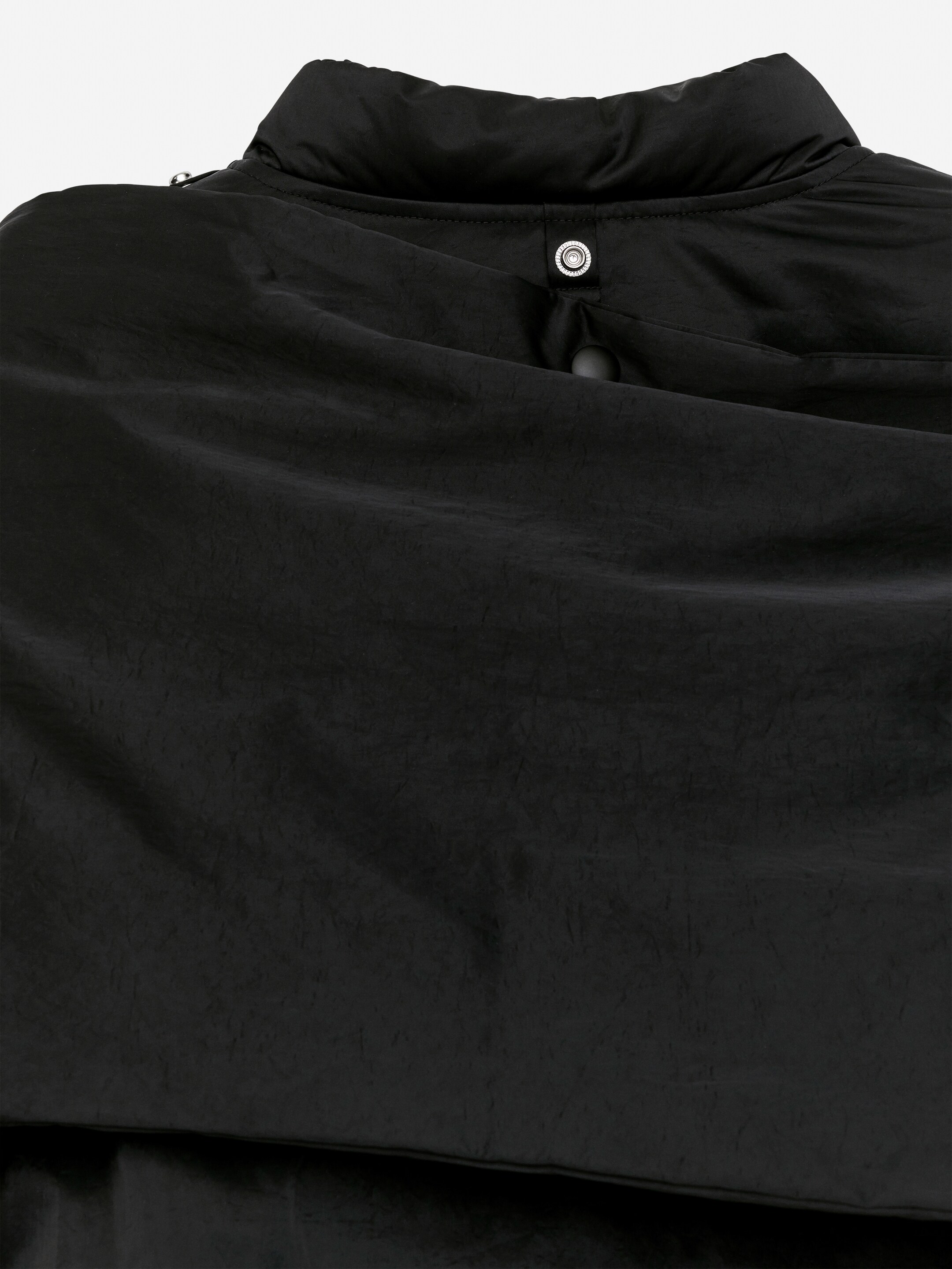 Vis større bilde: Baksiden av den svarte Upcycled Down Scarf Jacket vises, med sitt krøllete, polstrede stoff. En stående krage er synlig, sikret med en sølvfarget trykknapplukking.