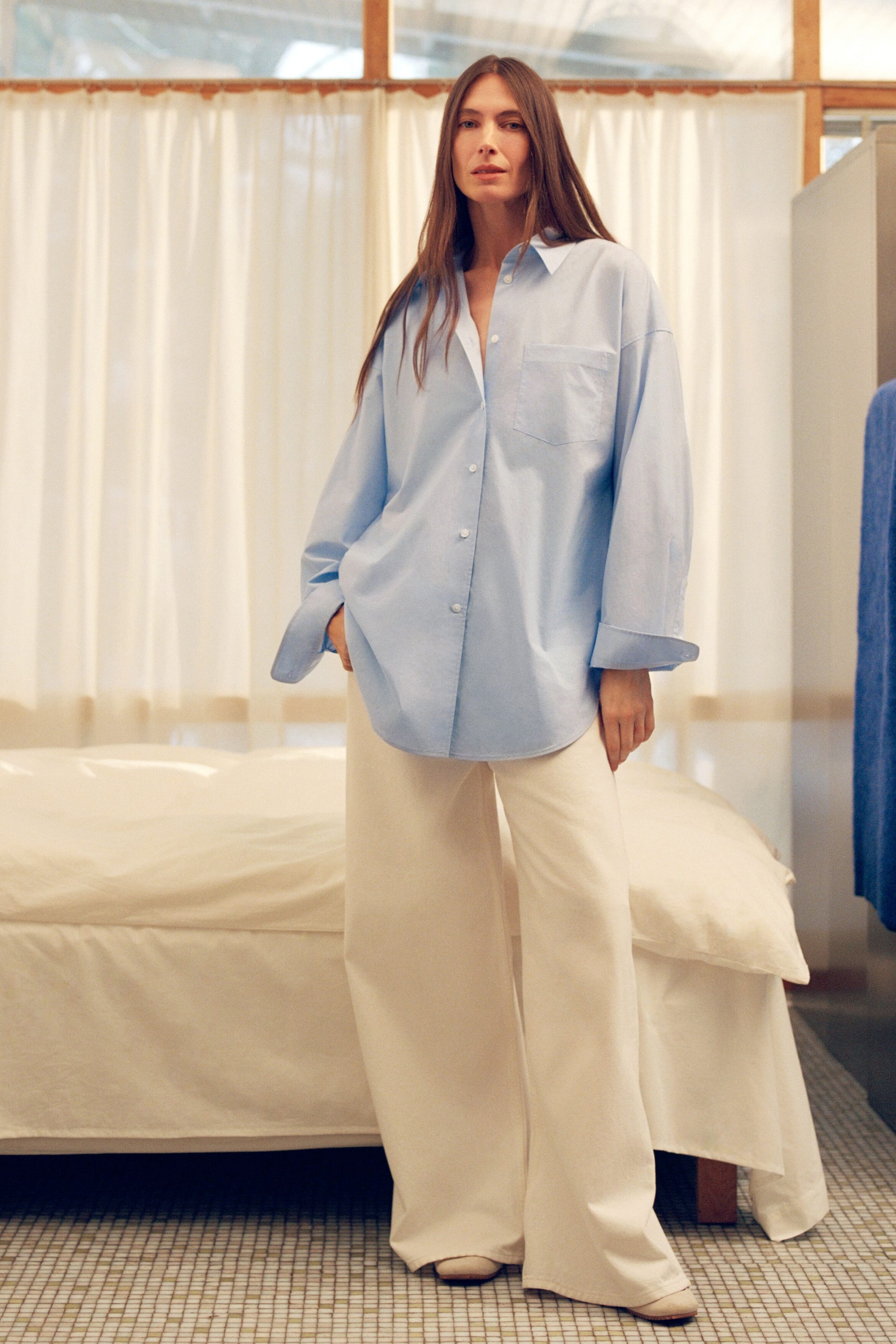 Ver imagen más grande: Una camisa azul claro de gran tamaño con botones al frente presenta un cuello en punta, botones blancos en la parte delantera y un único bolsillo parche en el pecho, y se combina con pantalones de pierna ancha de color crema que ofrecen un ajuste suelto y fluido.