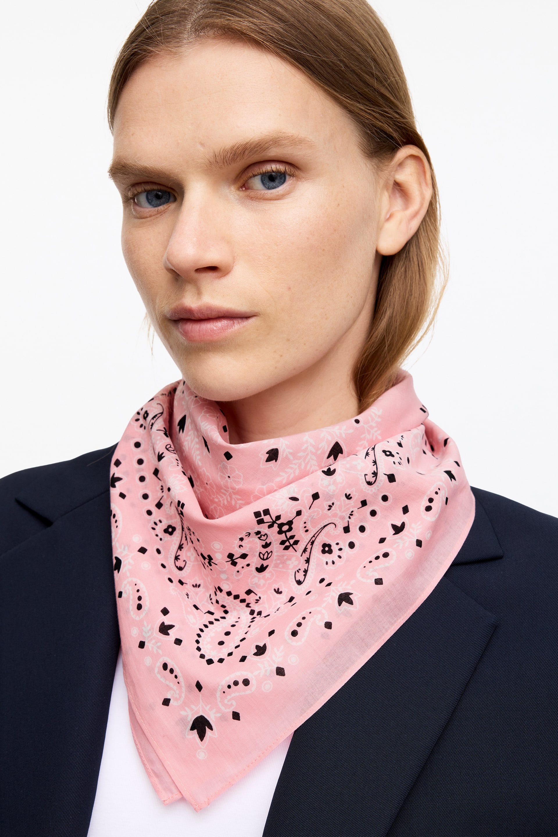 Vis større bilde: Det rosa bandanaen er knyttet rundt halsen, med svarte og hvite paisley-lignende motiver og små prikker. Den er stylet over en hvit topp og under en marineblå blazer.