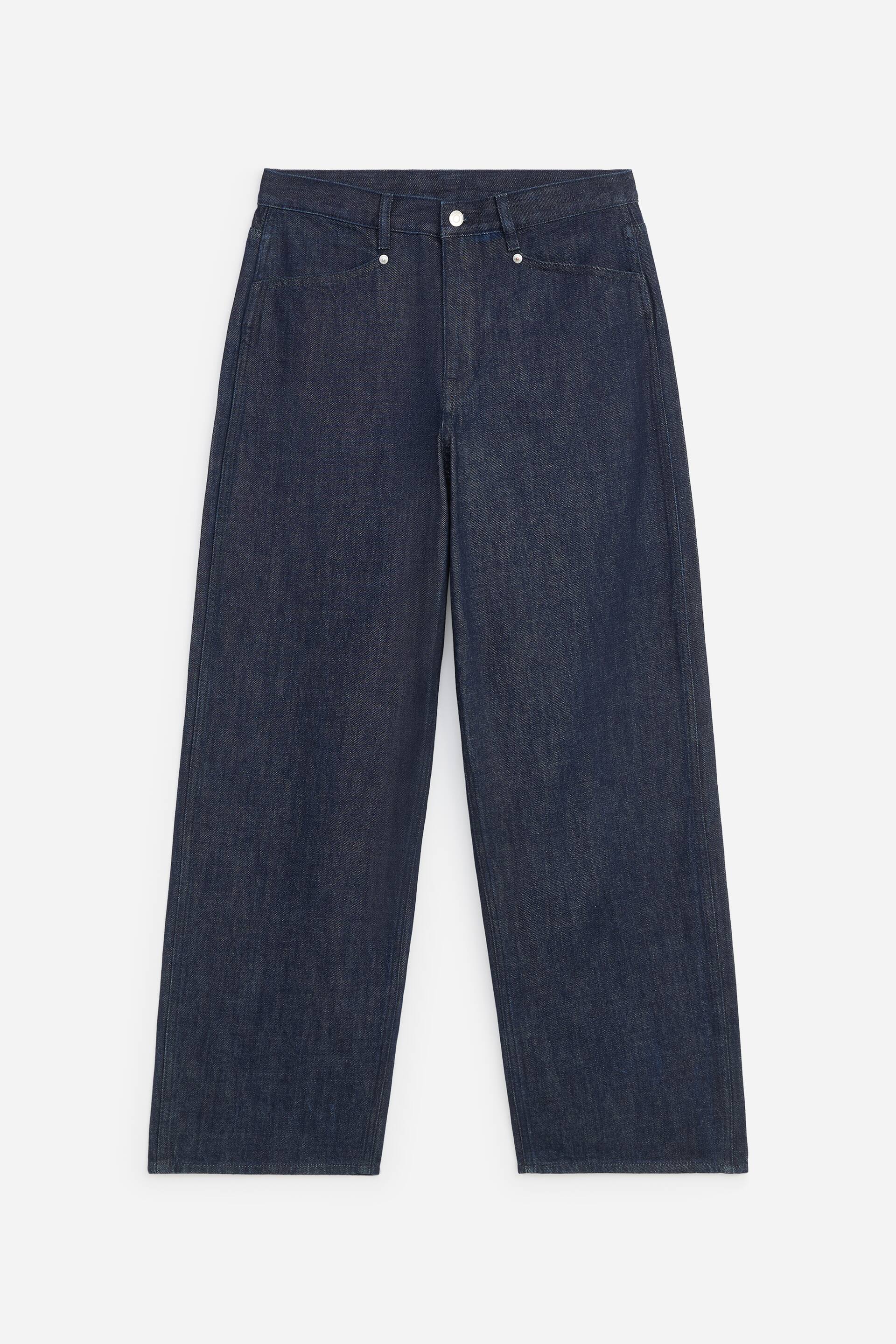 Agrandir l'image: Un jean large en denim indigo foncé est présenté de face, mettant en valeur une taille haute avec une fermeture à bouton effet argenté et des passants de ceinture. Le modèle présente des poches italiennes à l’avant avec des rivets métalliques et des jambes droites et larges.