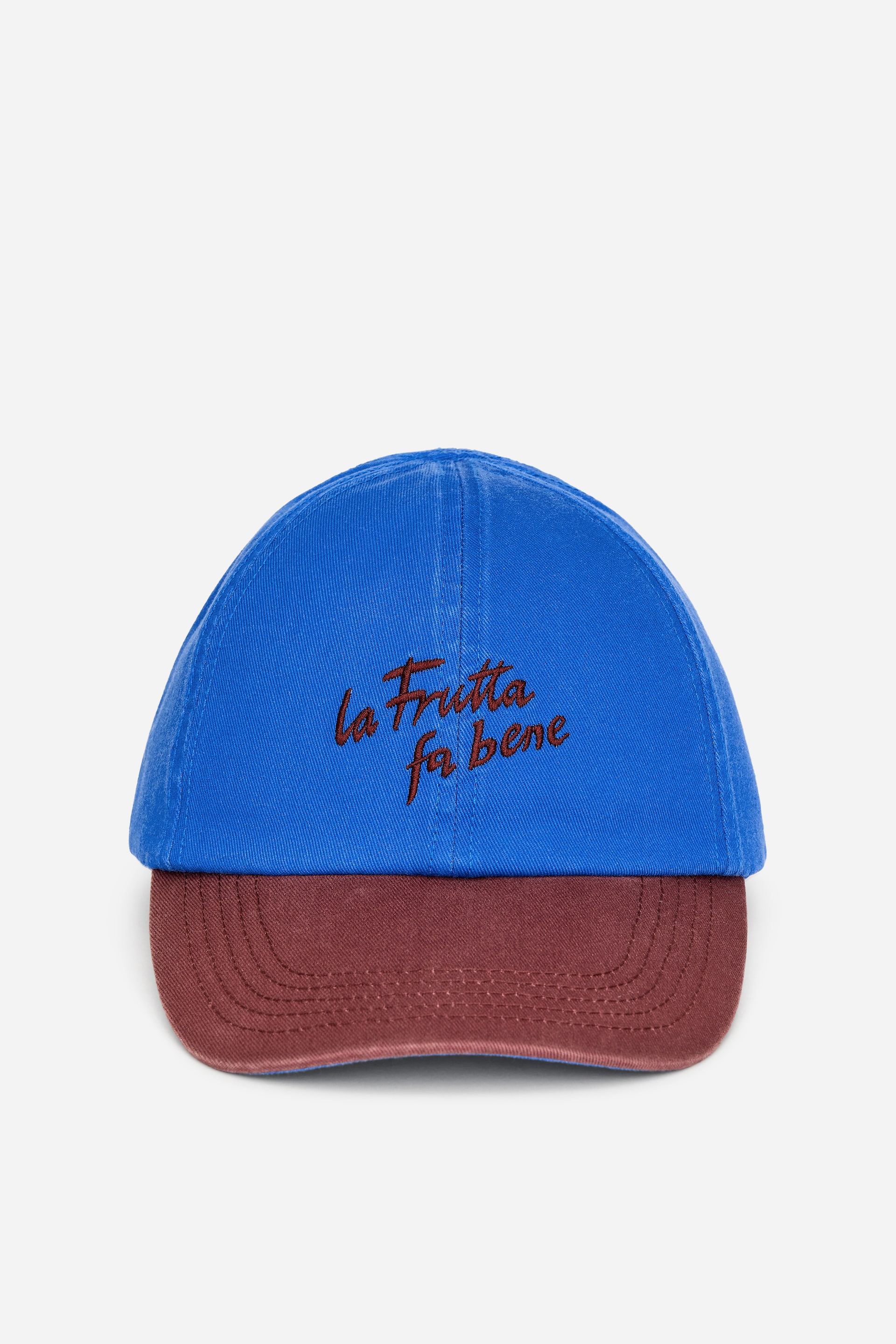 Agrandir l'image: Une casquette est présentée de face, mettant en avant une couronne en sergé de coton bleu à 6 panneaux et une visière bordeaux avec des coutures apparentes. Le texte brodé en rouge, "la frutta fa bene", apparaît sur le devant de la couronne.