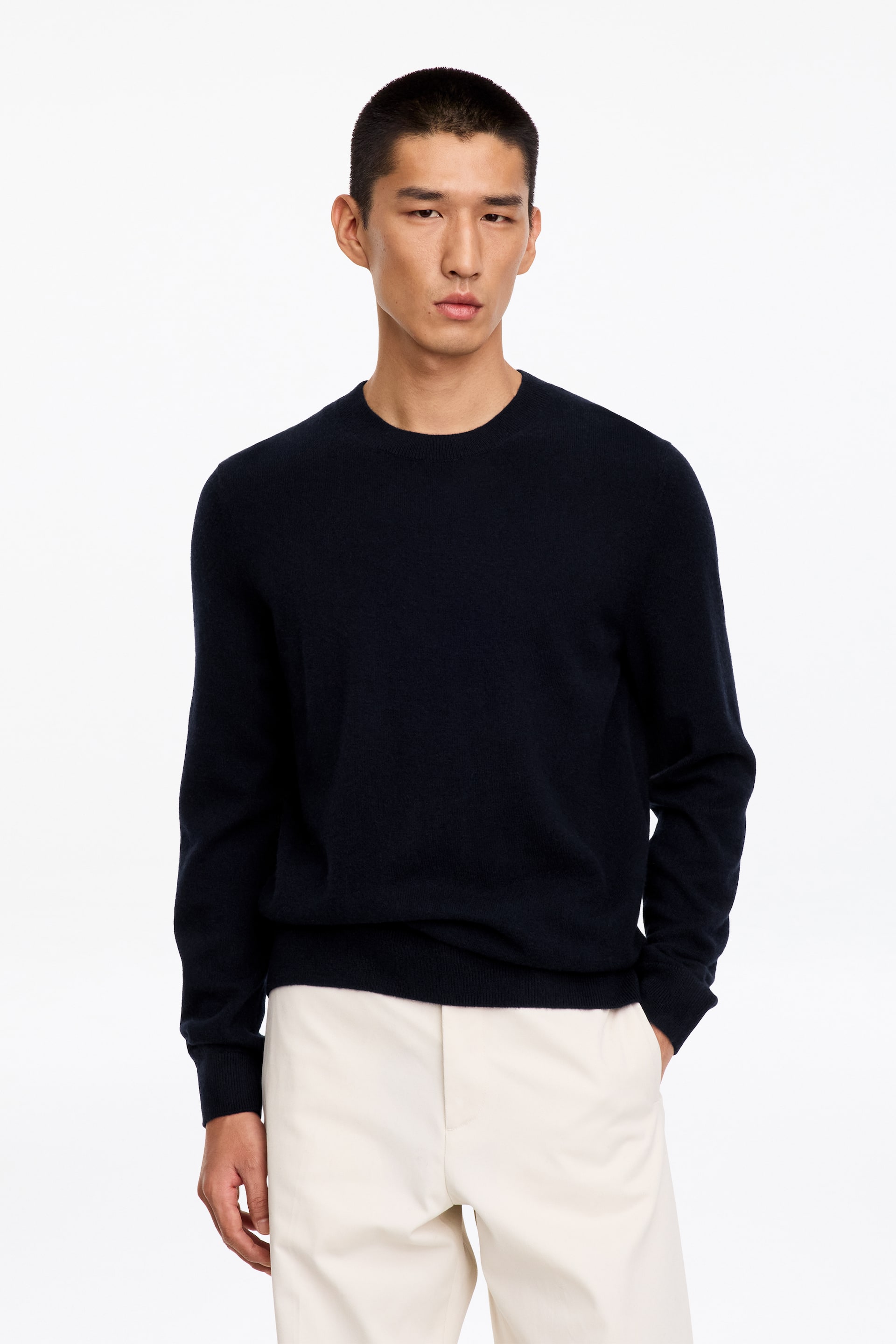 Größeres Bild anzeigen: Ein marineblauer Rundhalspullover wird vom Model getragen und mit cremefarbenen Hosen kombiniert. Der langärmelige Strickpullover verfügt über Rippdetails am Kragen, an den Ärmelbündchen und am Saum.