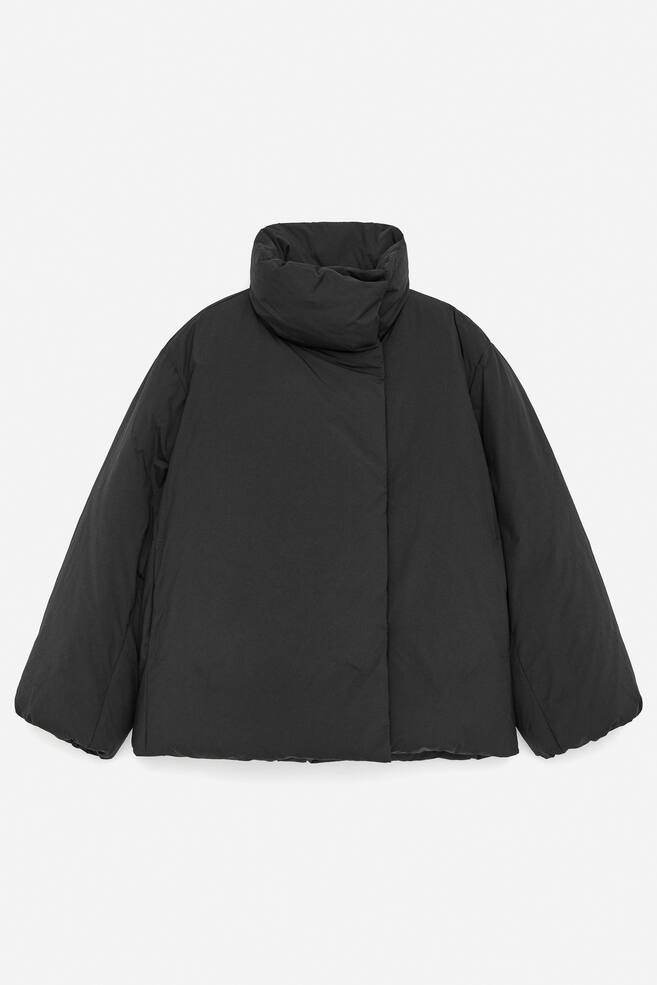 A black puffer jacket is being presented from the FRONT, designed with a high standing collar that is secured by a button closure, a hidden press button placket running down its front, and hidden pockets integrated into its side seams. - 1