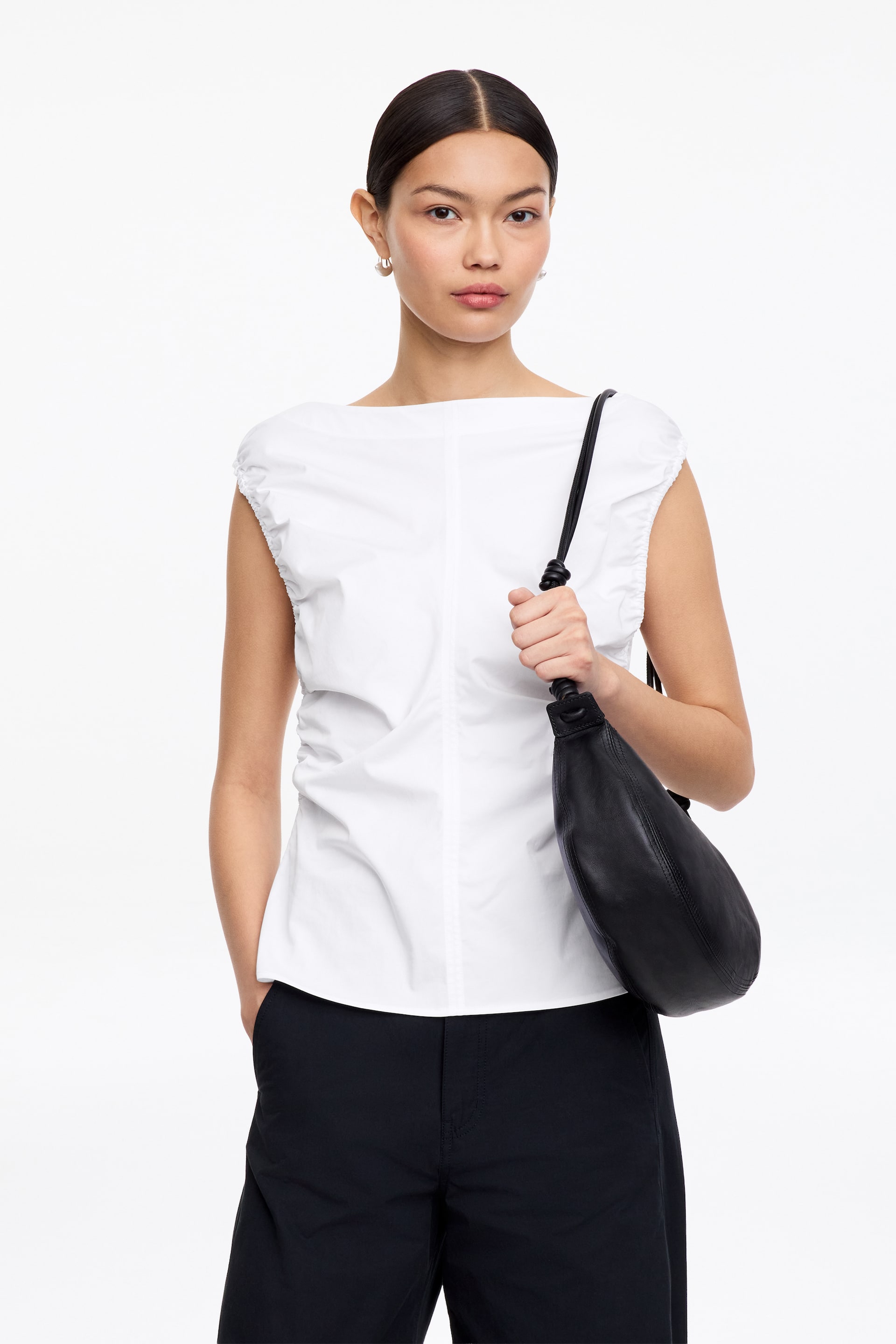 Zobacz większy obraz: Biały top bez rękawów z szerokim dekoltem typu łódka, marszczonymi rękawkami, pionowymi szwami i bocznymi marszczeniami.