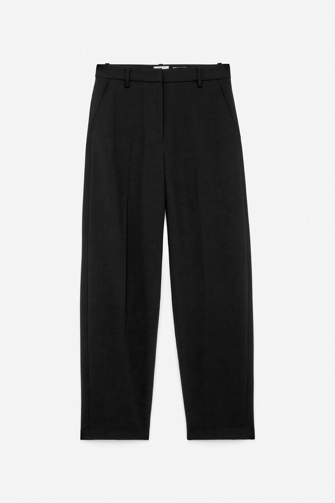 Black tailored trousers are being displayed from the FRONT, featuring prominent press creases, slanted side pockets, and a zip fly with button closure. They are designed in a cropped style. - 1