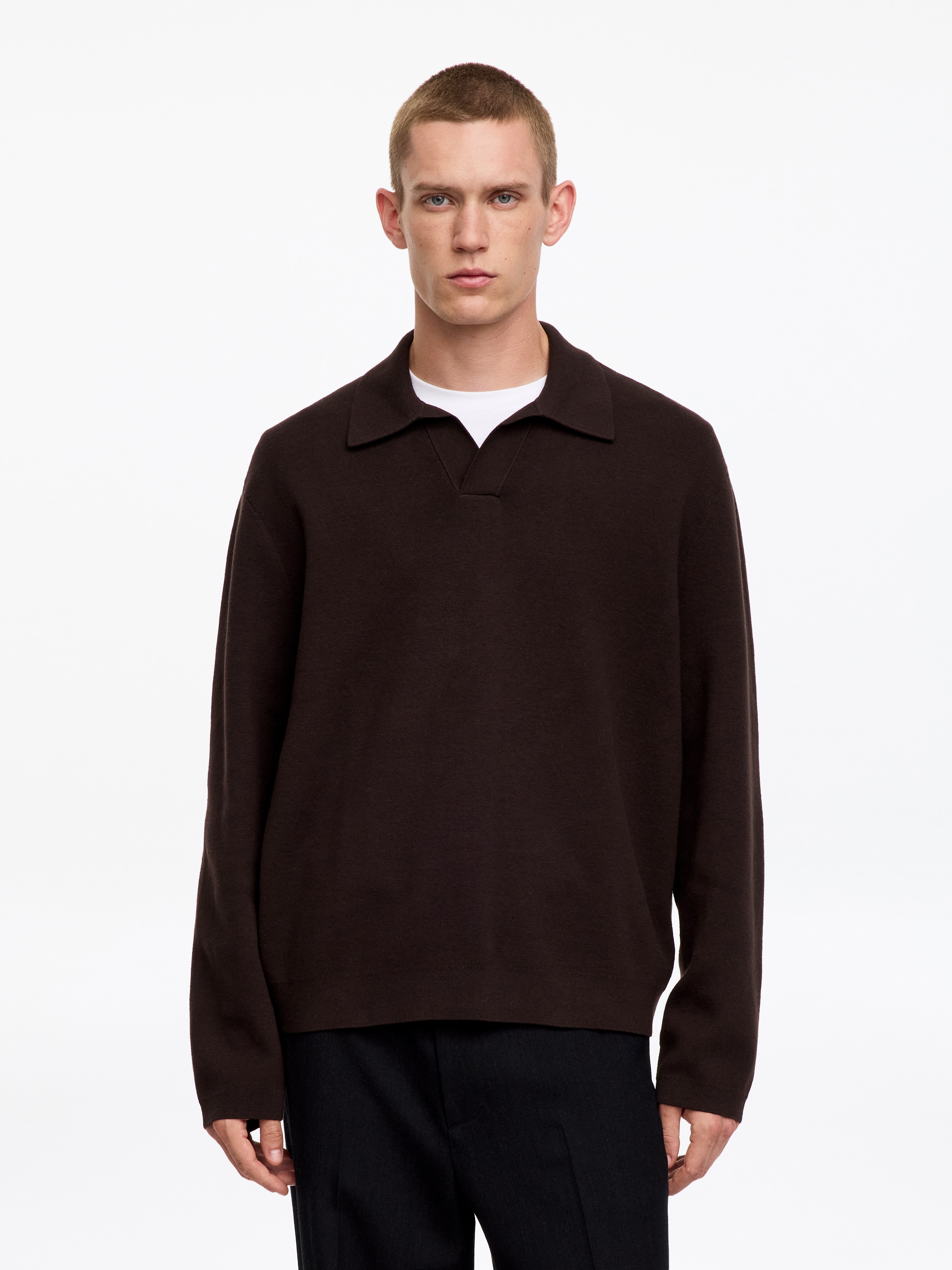 Una maglia polo a maniche lunghe in maglia marrone scuro presenta un colletto con scollo a V aperto e una chiusura a bottoni, con maniche lunghe e orlo dritto, presentata dal FRONTE.