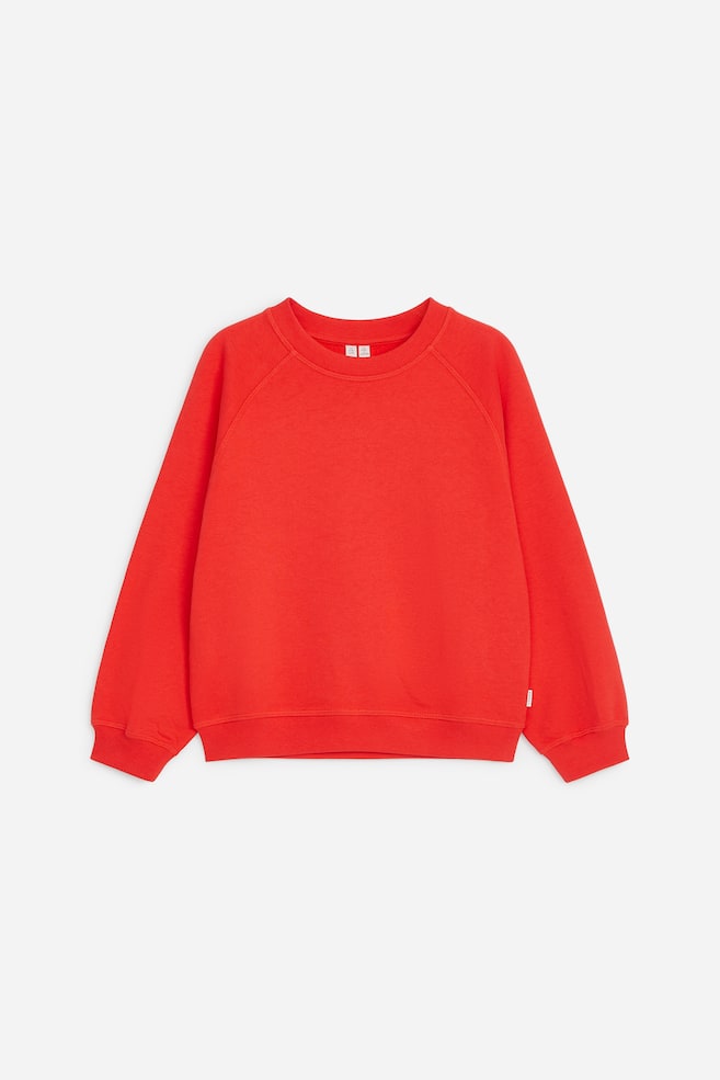 Una felpa rossa in cotone è mostrata frontalmente, con classico girocollo e maniche raglan. Presenta una vestibilità rilassata con bordi a coste su scollo, polsini e fondo. - 1