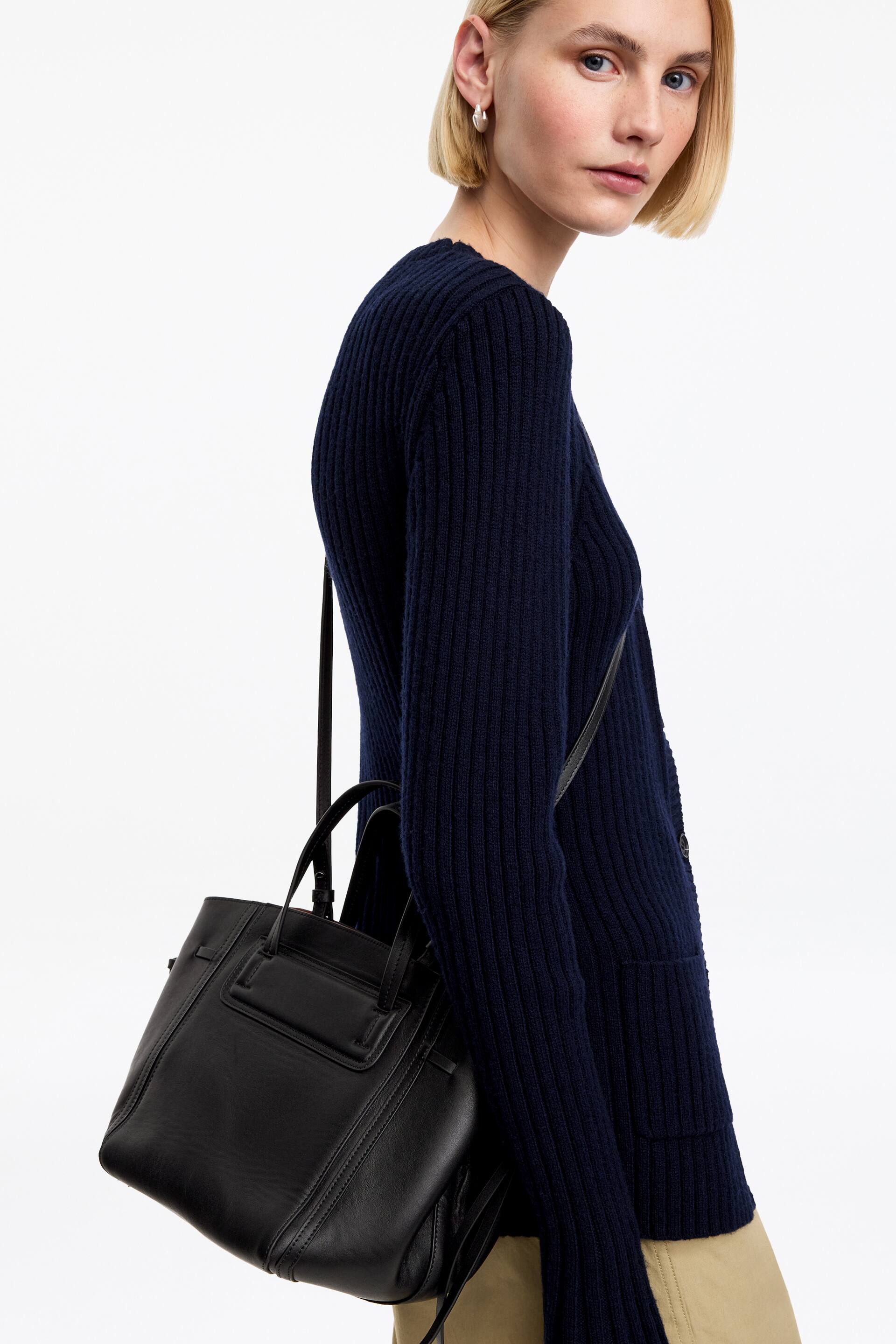 Visa större bild: Den marinblå ribbstickade koftan har en knappfrontdesign med långa ärmar och en påsydd ficka, bärs över ett lättare plagg och ses från en sned framvinkel. Den har en ribbad struktur genomgående och en rund halsringning.