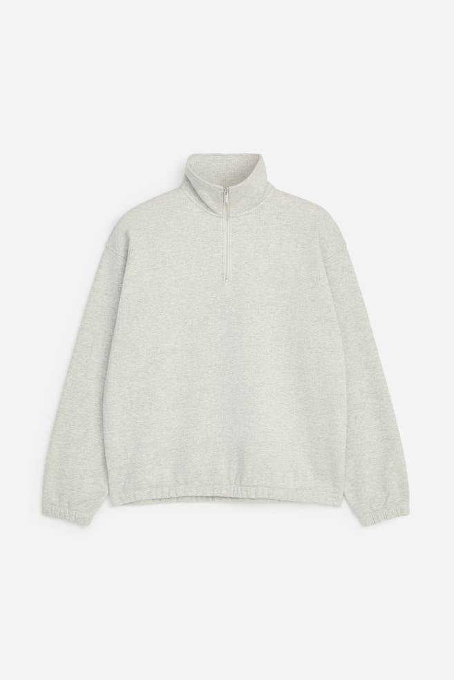 Ein hellgrauer melierter Half-Zip-Sweatshirt ist von vorne zu sehen und verfÃ¼gt Ã¼ber einen hohen Stehkragen mit silberfarbenem ReiÃverschluss. Das Sweatshirt zeigt Ã¼berschnittene Schultern, lange Ãrmel mit elastischen BÃ¼ndchen und einen gerafften, elastischen Saum. - 1