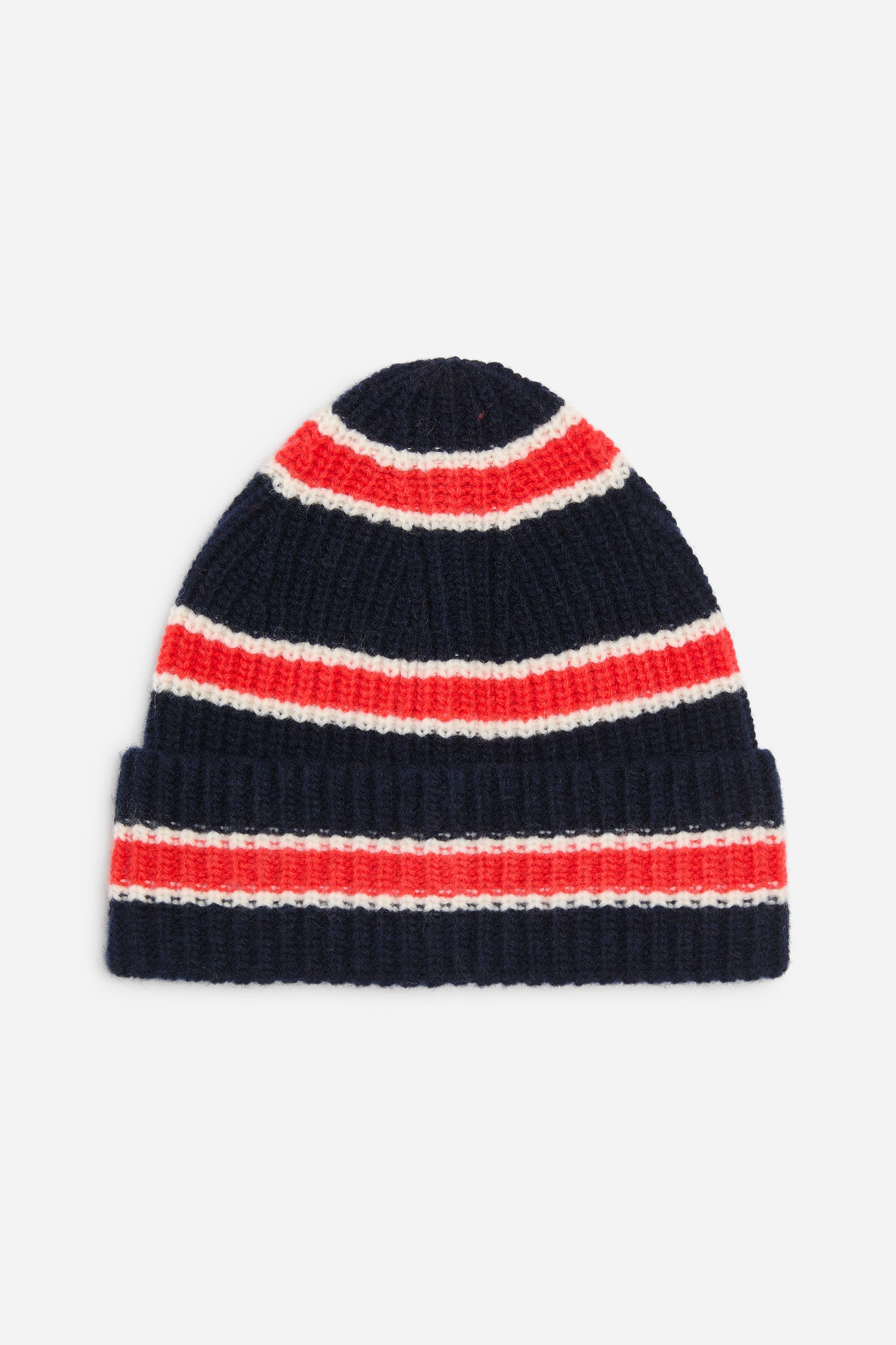 View larger image: A rib-knitted beanie is lying flat from a front angle, showcasing a chunky knit style with a wide turn-up brim. The beanie features a navy blue base accented with horizontal stripes of red and white.