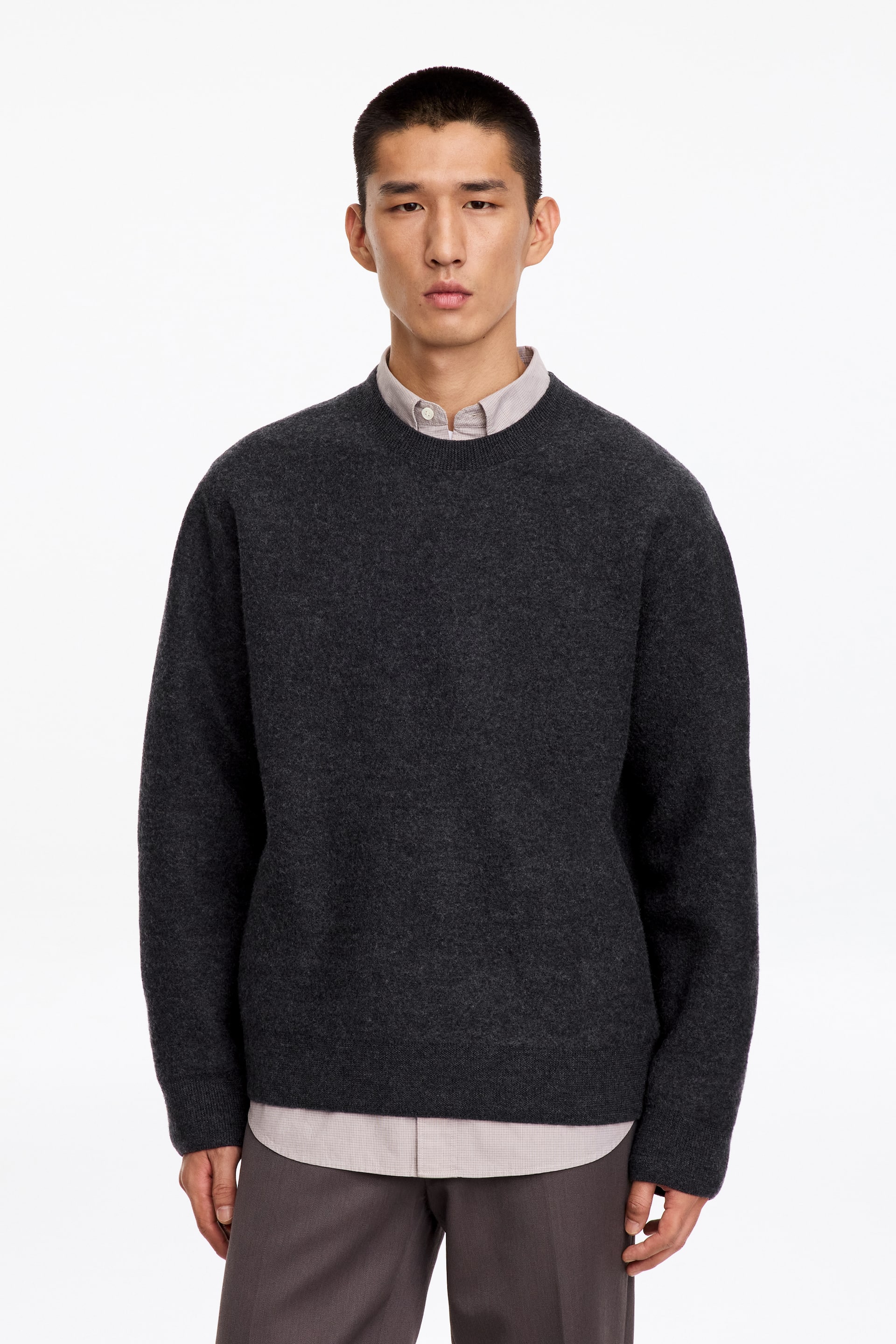 Größeres Bild ansehen: Der/die Model trägt einen anthrazitgrauen Rundhalspullover über einem hellen Hemd mit Kragen und dunkler Hose. Der Pullover verfügt über eine strukturierte Strickkonstruktion mit Rippdetails am Ausschnitt, an den Bündchen und am Saum.