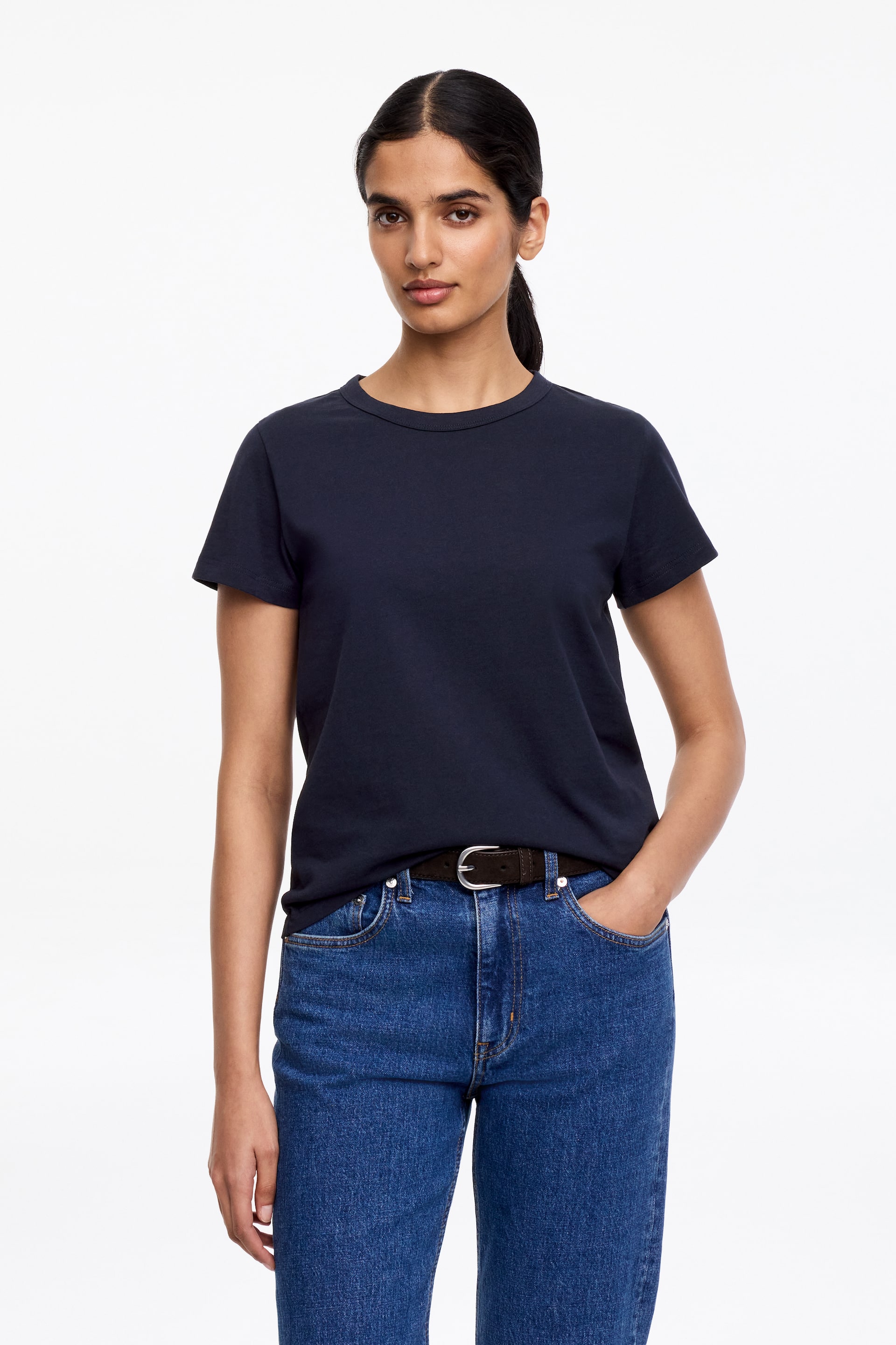 Agrandir l'image: Un t-shirt bleu marine à manches courtes est présenté de face, avec un col rond, et est porté rentré dans un jean bleu.