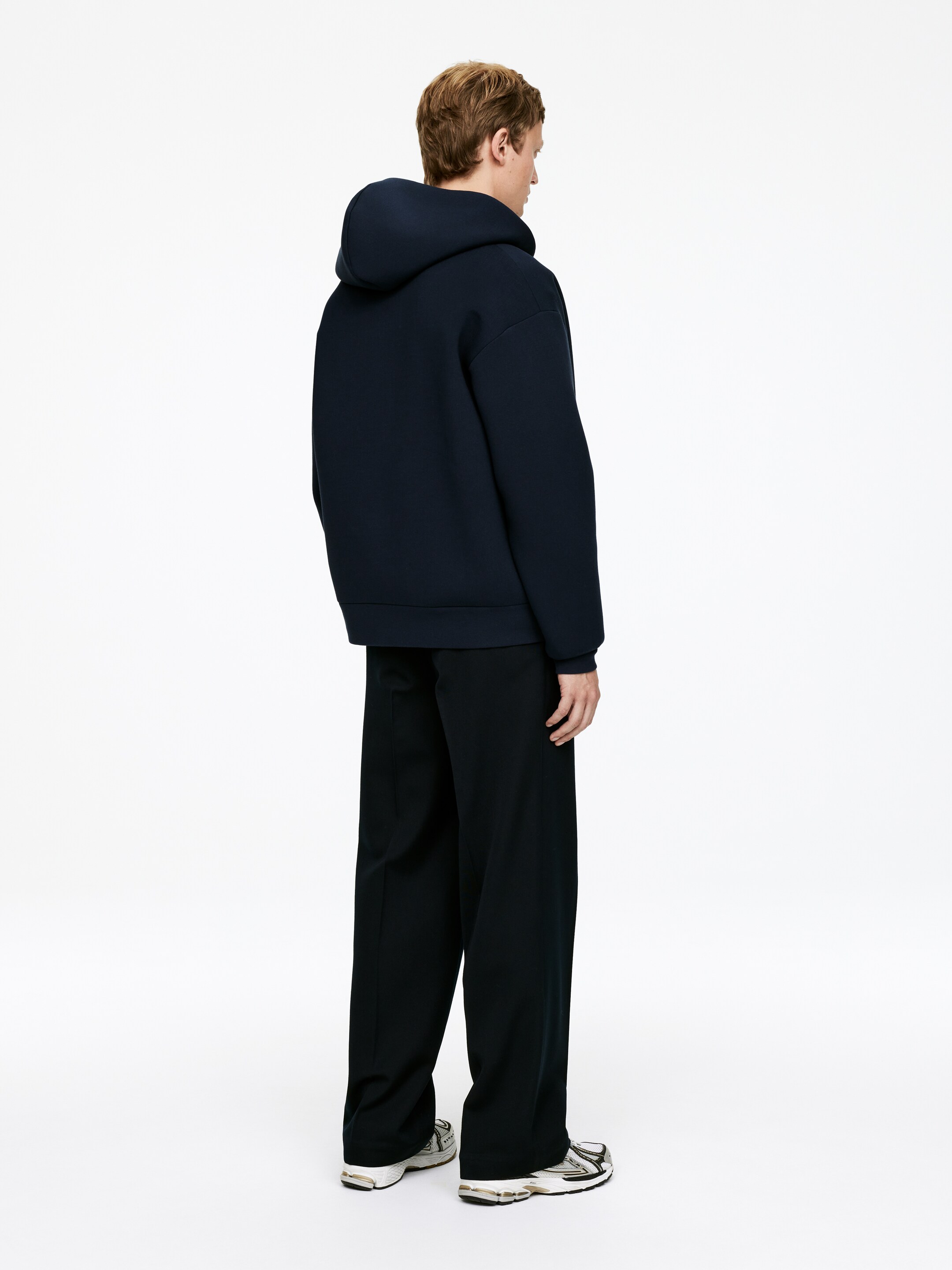 Grotere afbeelding bekijken: Een hoodie met rits, genaaid van een rekbare scuba-stof, wordt door het model gedragen. Het heeft een capuchon van schelpstof, geribbelde manchetten en een geribbelde zoom, gesneden in een ontspannen pasvorm.