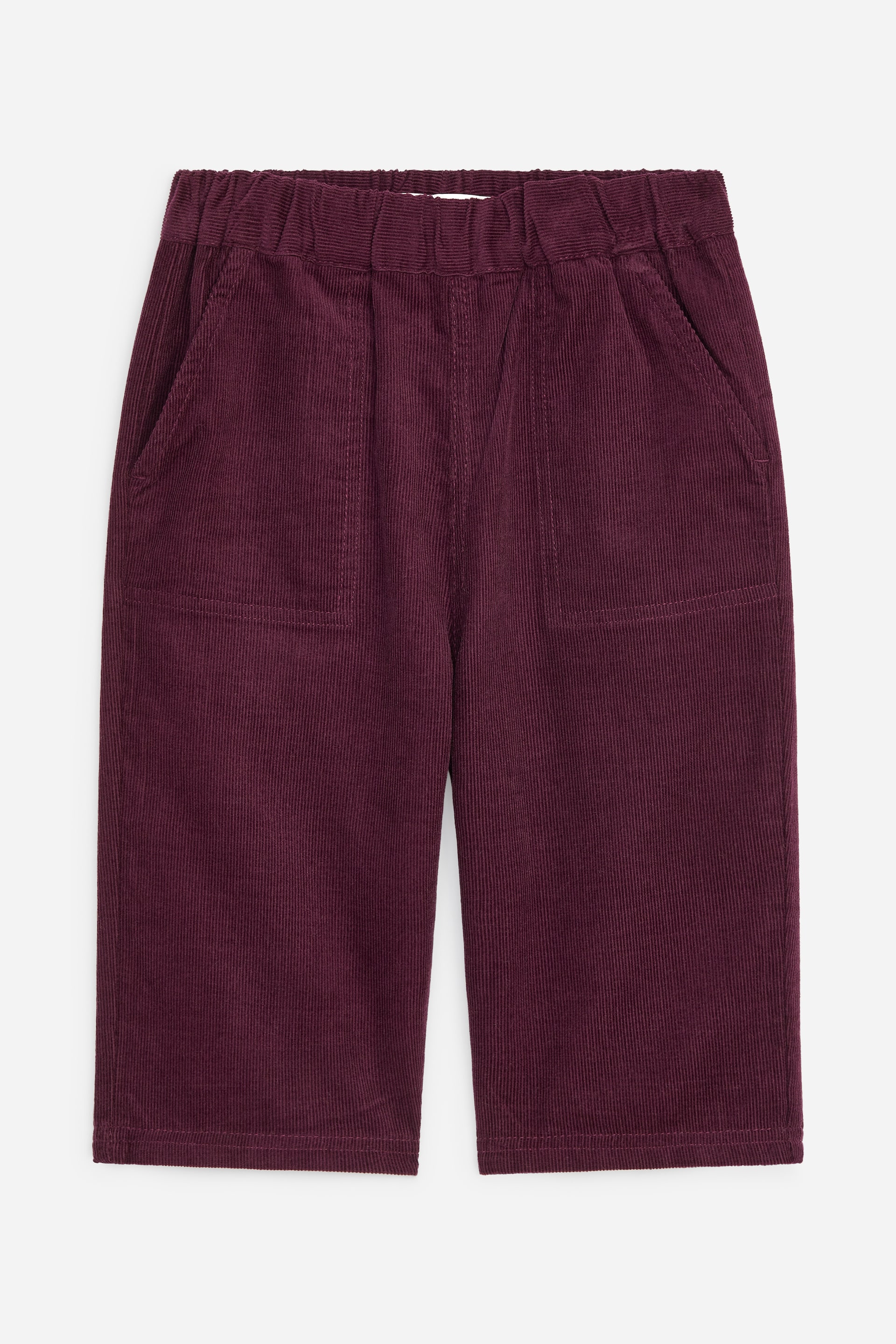 Visualizza immagine più grande: Pantaloni in velluto a coste di un intenso colore bordeaux sono disposti in piano, rivolti verso l'alto. Presentano una vita elasticizzata, due tasche laterali oblique e due tasche applicate rettangolari sul davanti delle gambe.