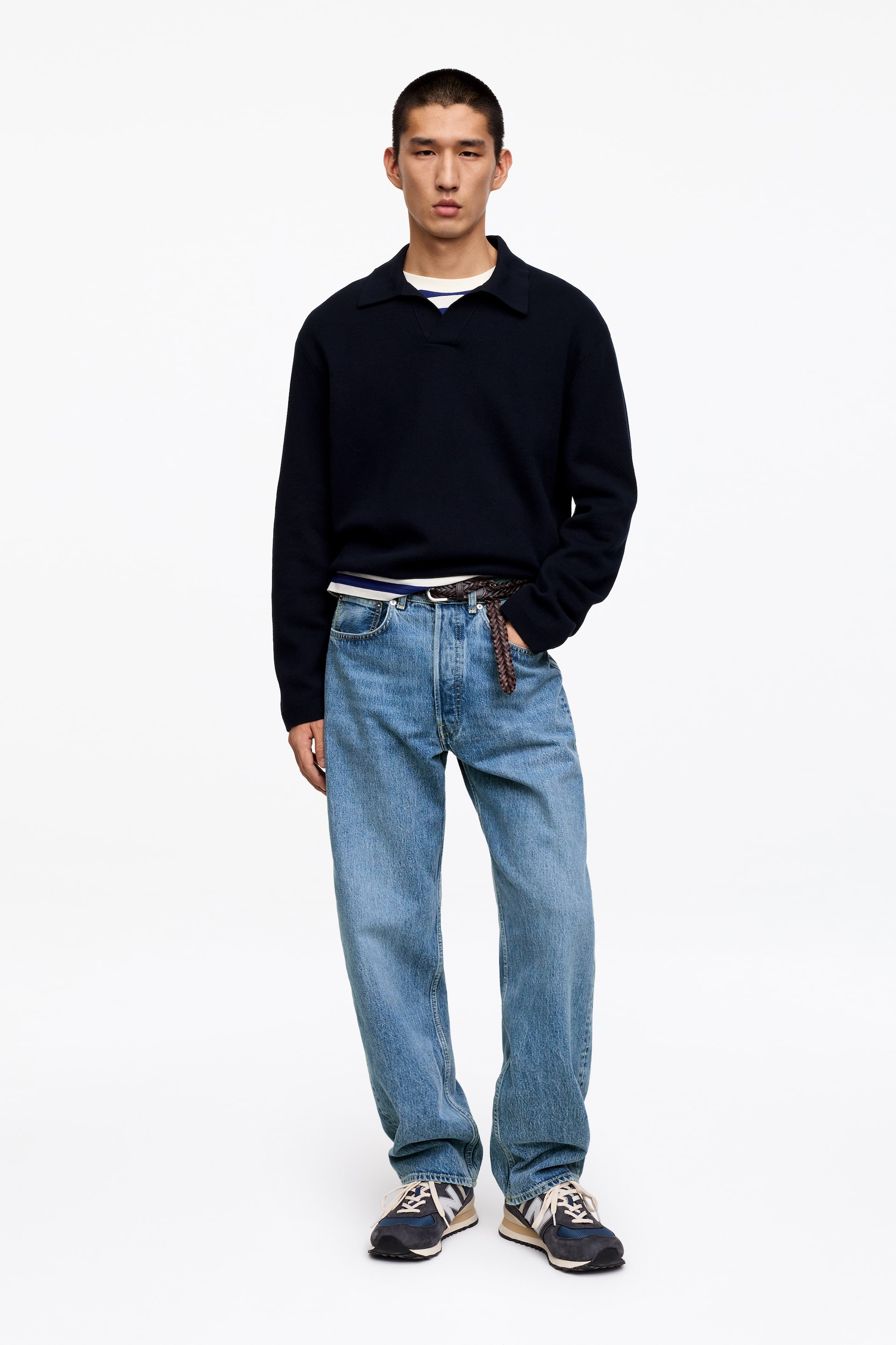 Agrandir l'image: Un pull polo bleu marine est présenté, avec un col évasé et une ouverture en V. Il est superposé sur un t-shirt blanc, visible au niveau de l'encolure et de l'ourlet.