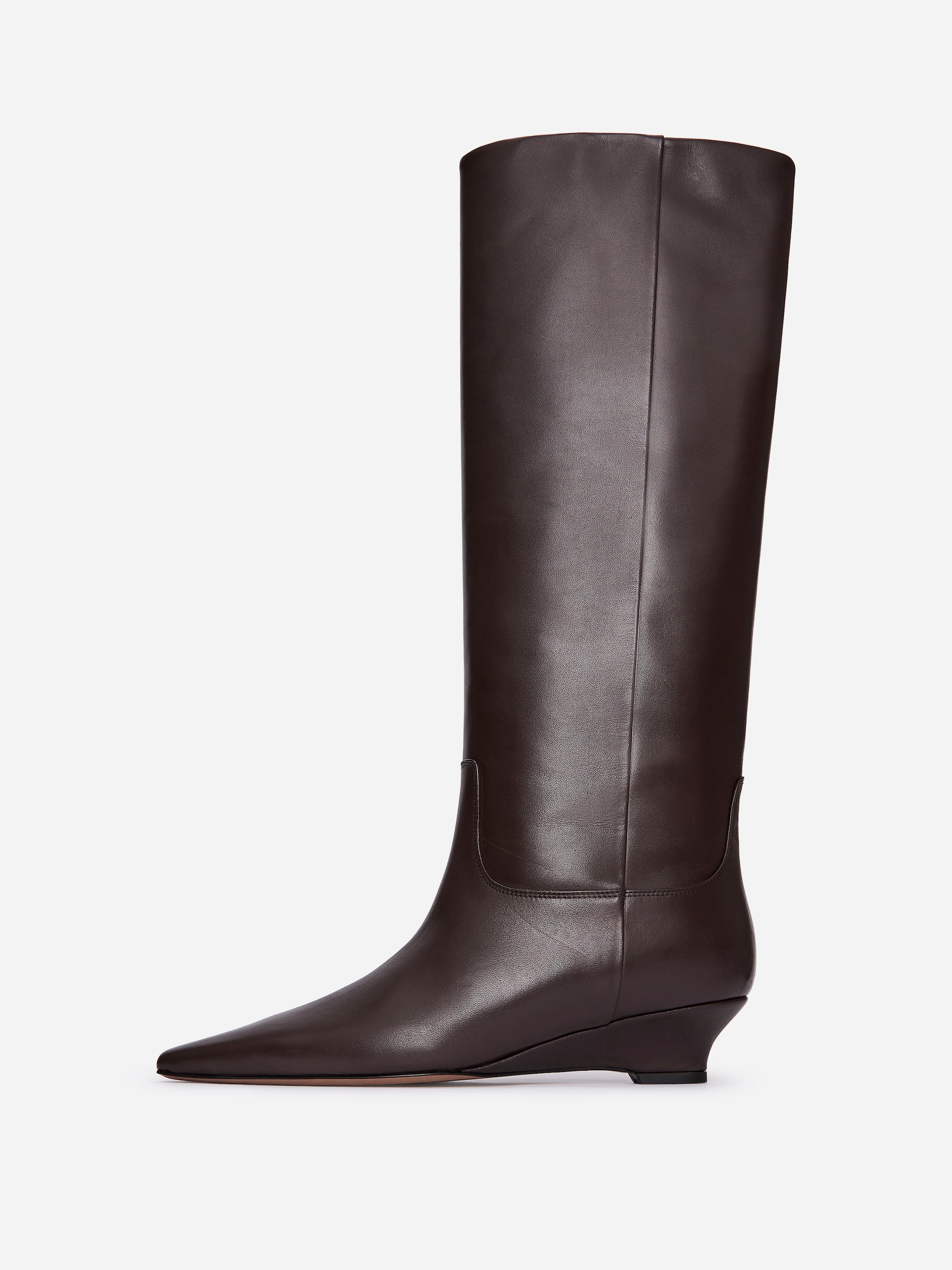 Agrandir l'image: Une botte haute en cuir brun foncé est orientée vers la droite, avec un bout pointu et un talon compensé bas. Elle est conçue avec une finition lisse et une tige droite, mettant en valeur une couture visible qui remonte le devant.