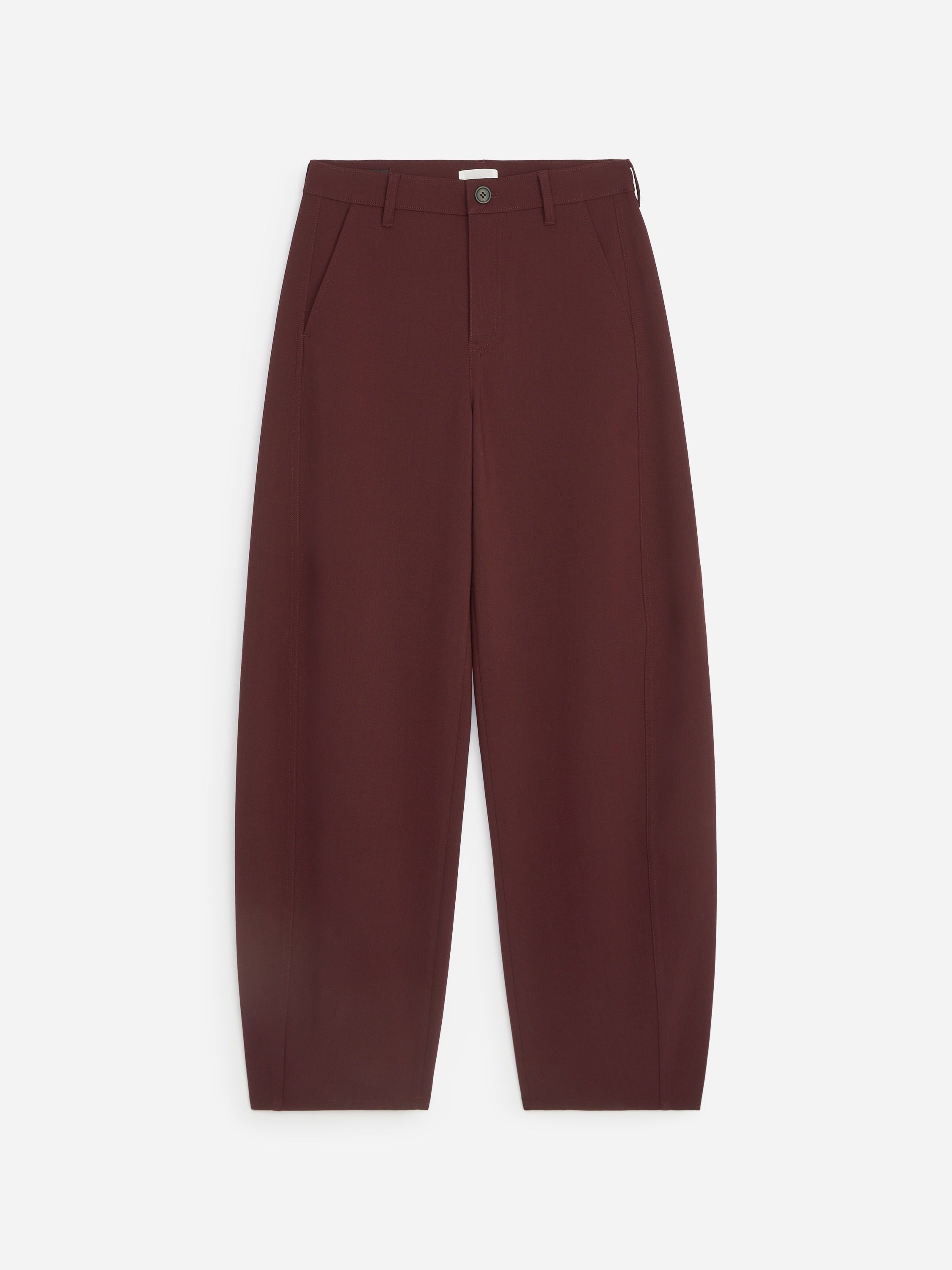 Un pantalon marron en mélange de laine, doté d’une silhouette décontractée à jambes barrel incurvées, est porté par le mannequin, qui se tient debout avec une main glissée dans la poche latérale. Le pantalon est associé à une ceinture en cuir noire, à un haut bordeaux à manches longues et à des chaussures plates noires.