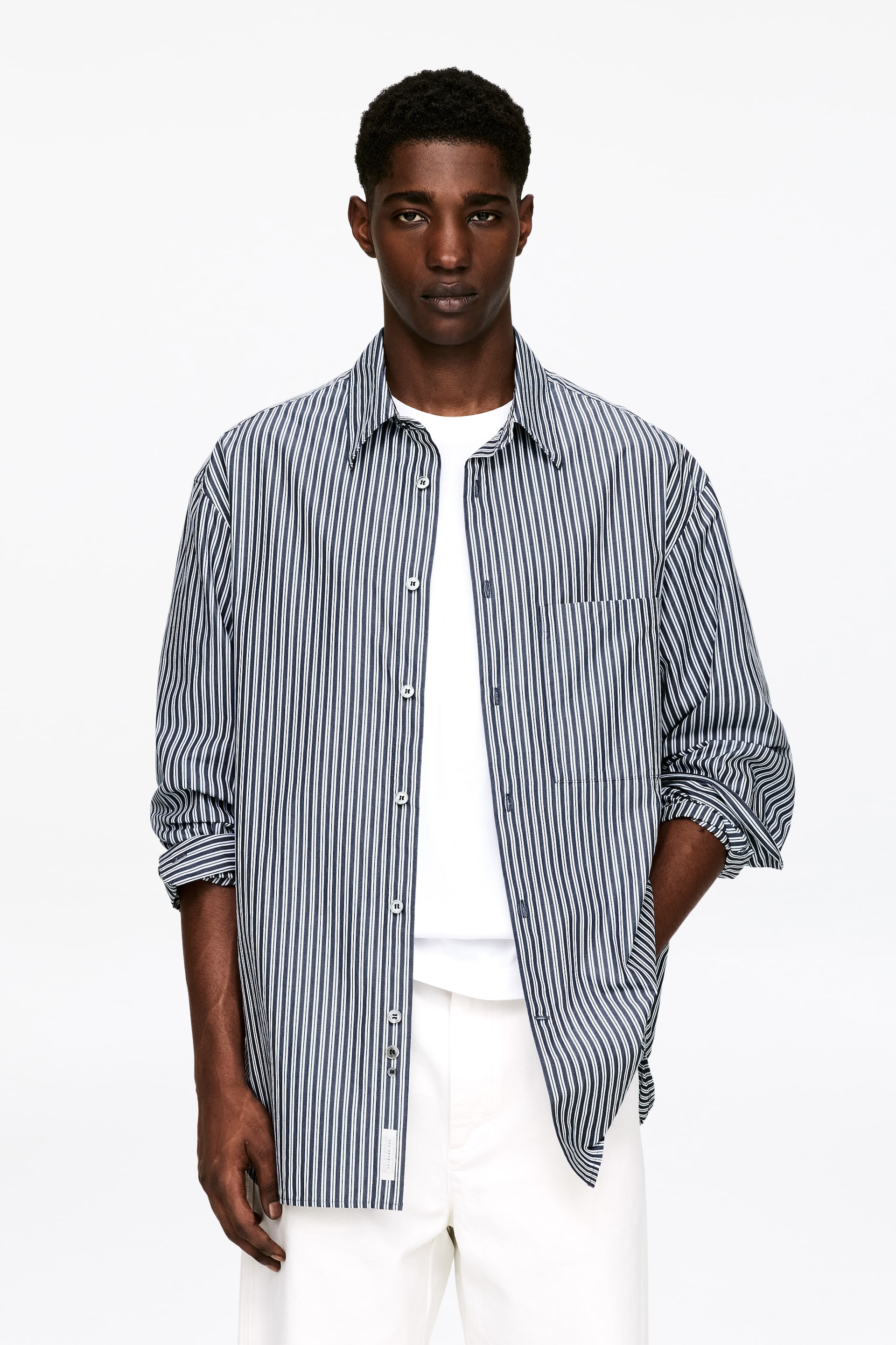 Größeres Bild ansehen: Ein grün-weiß gestreiftes Hemd mit Knopfleiste ist nach vorne gerichtet und zeigt einen spitzen Kragen, eine aufgesetzte Brusttasche links und hochgekrempelte lange Ärmel. Es wird offen über einem weißen Rundhals-T-Shirt getragen.
