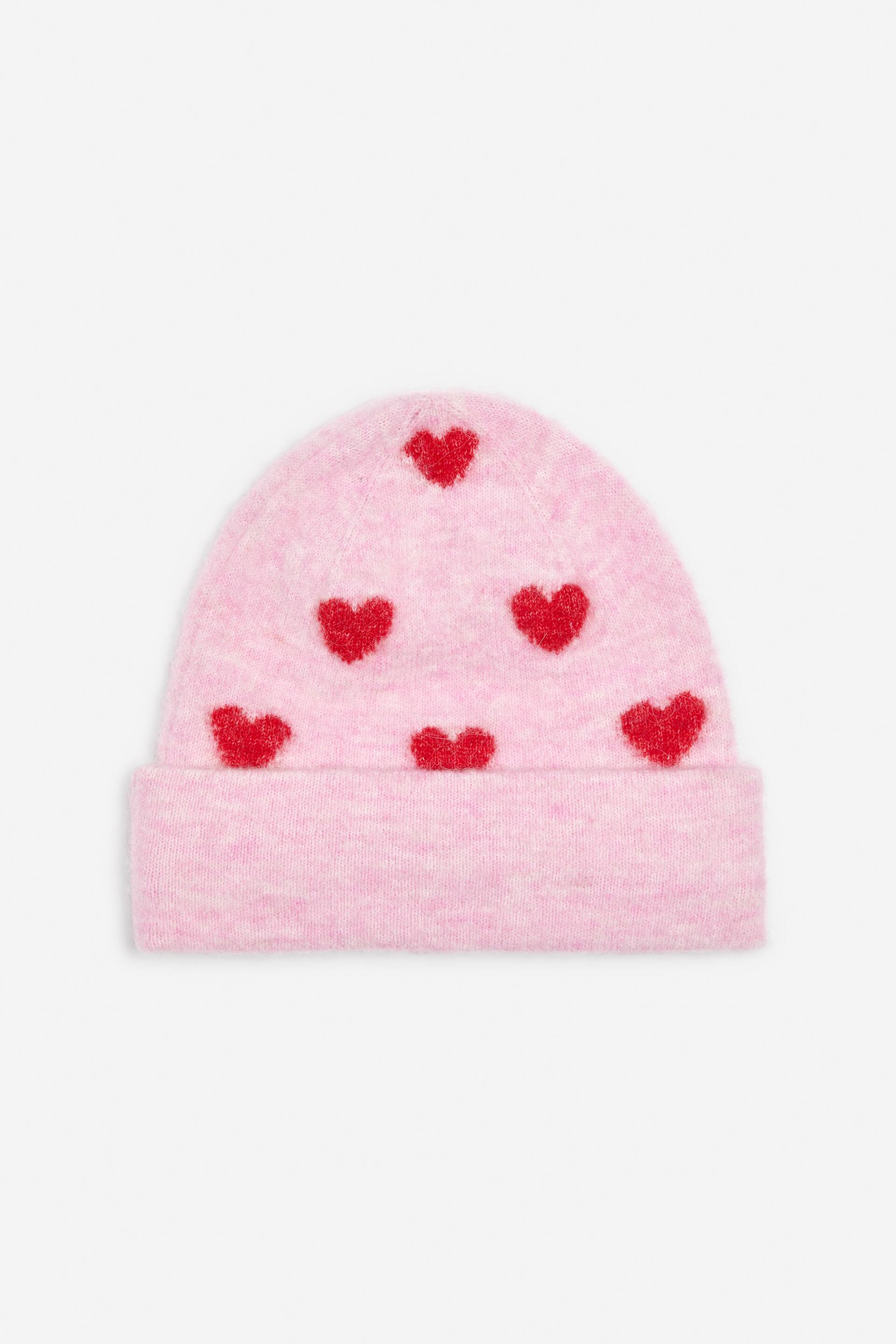 Visualizza l'immagine ingrandita: Un berretto lavorato a maglia di colore rosa chiaro è rivolto in avanti, caratterizzato da una texture morbida e da diversi motivi a cuore rosso sulla sua corona. Presenta un bordo ripiegato nella parte inferiore.