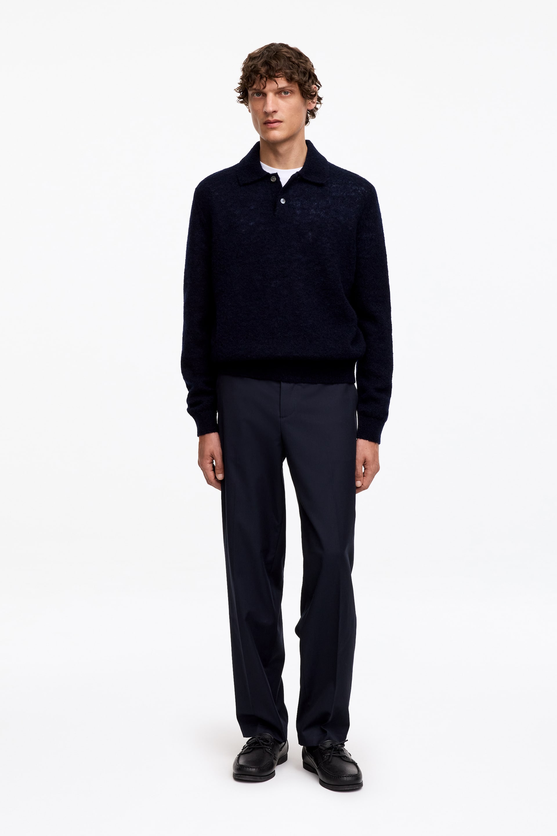 Größeres Bild ansehen: Ein marineblauer Polopullover wird frontal präsentiert. Er verfügt über eine strukturierte Strickoptik, einen Polokragen und eine Zweiknopfleiste und wird über einem weißen T-Shirt mit Rundhalsausschnitt getragen.
