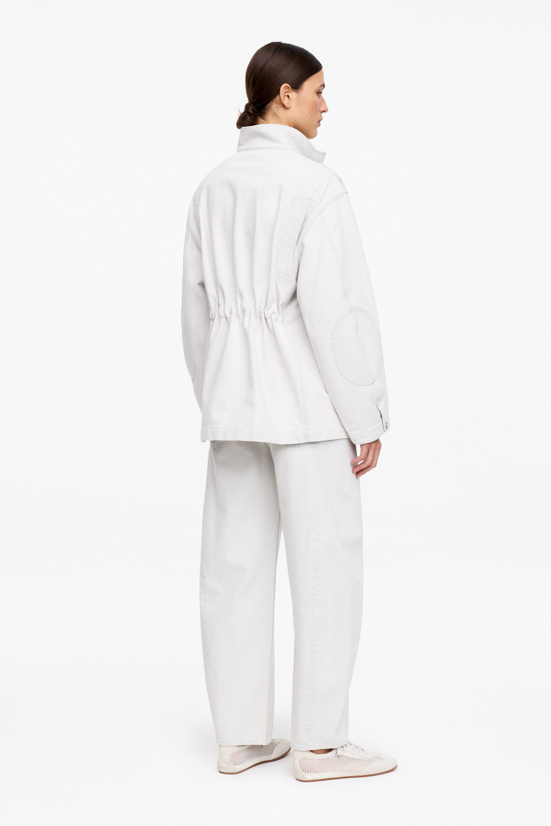 Ver imagen más grande: Una chaqueta utilitaria gris claro con cuello alto, cintura fruncida con cordón y parches circulares en los codos, combinada con pantalones de pierna ancha a juego, vista desde atrás.