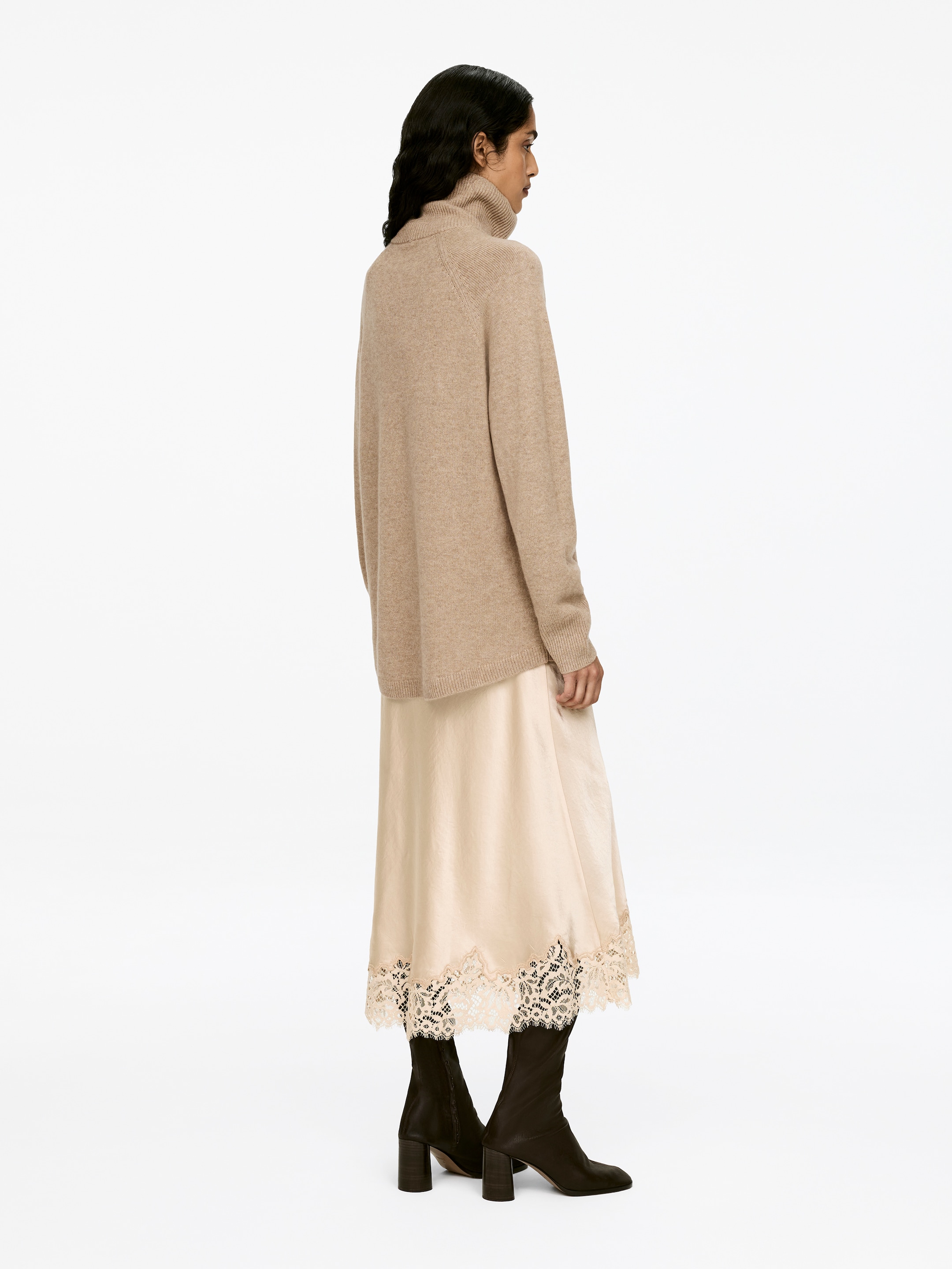 Visa större bild: En beige polotröja, tillverkad av kashmir och merinoull, bärs av modellen. Den har raglanärmar och ribbade kanter, och är stylad över en ljusfärgad underkjol med spetskant.