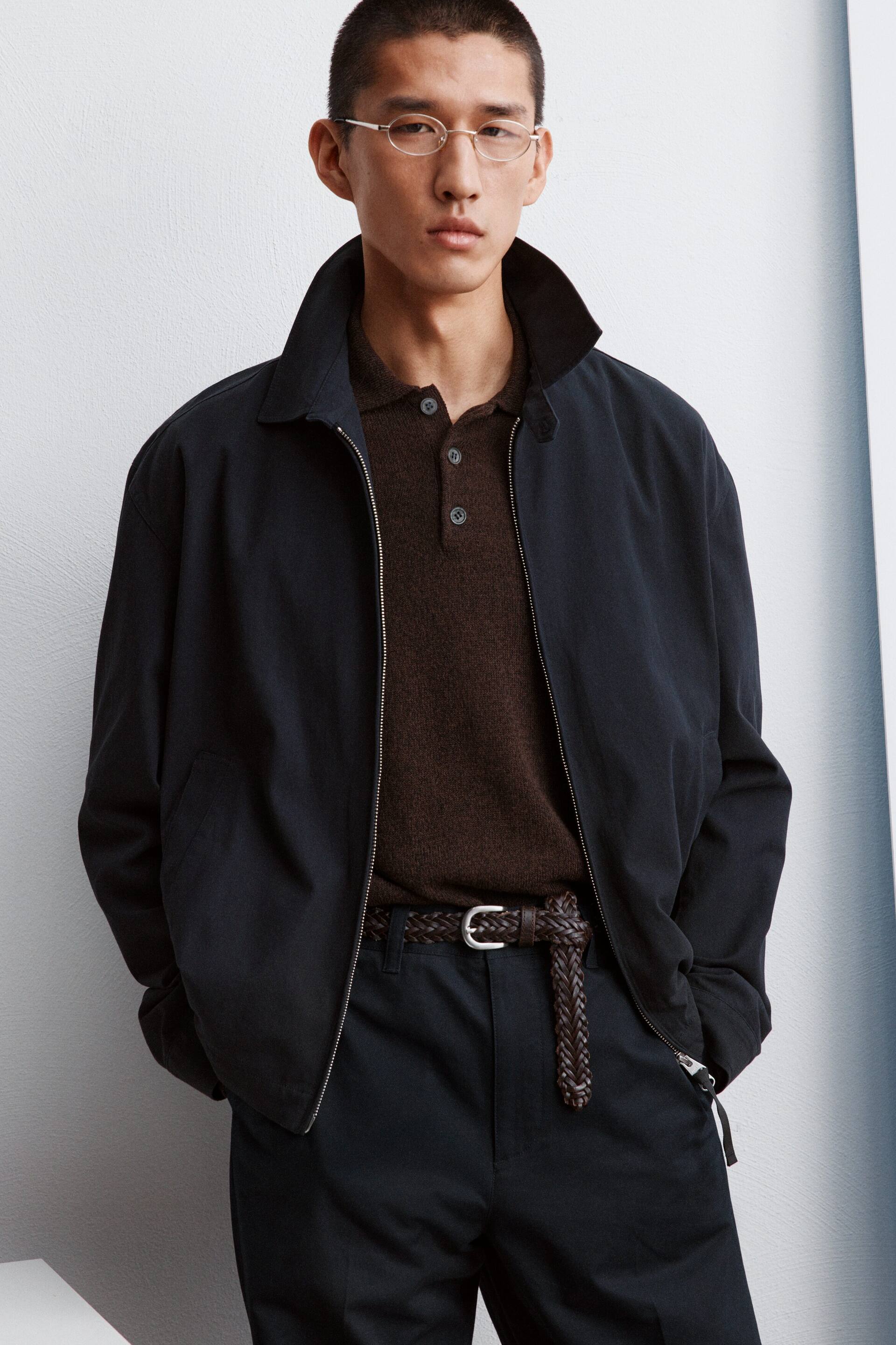 Visualizza immagine più grande: Una giacca stile bomber di un blu navy scuro è indossata, caratterizzata da un colletto aperto, tasche laterali e una cerniera argentata parzialmente aperta, che rivela una polo in maglia marrone sottostante.