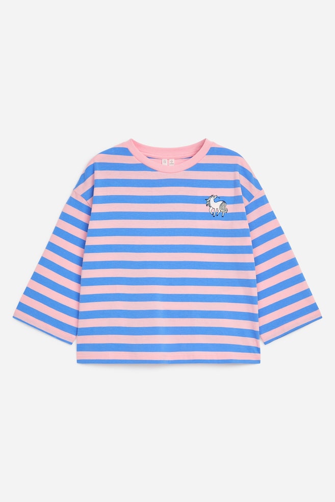 En pink og blå T-shirt med vandrette striber vises i en afslappet pasform med dropped shoulders og brede 3/4-lange ærmer set forfra. T-shirten har en ensfarvet pink rund halsudskæring og en lille hvid enhjørning broderet på brystet. - 1