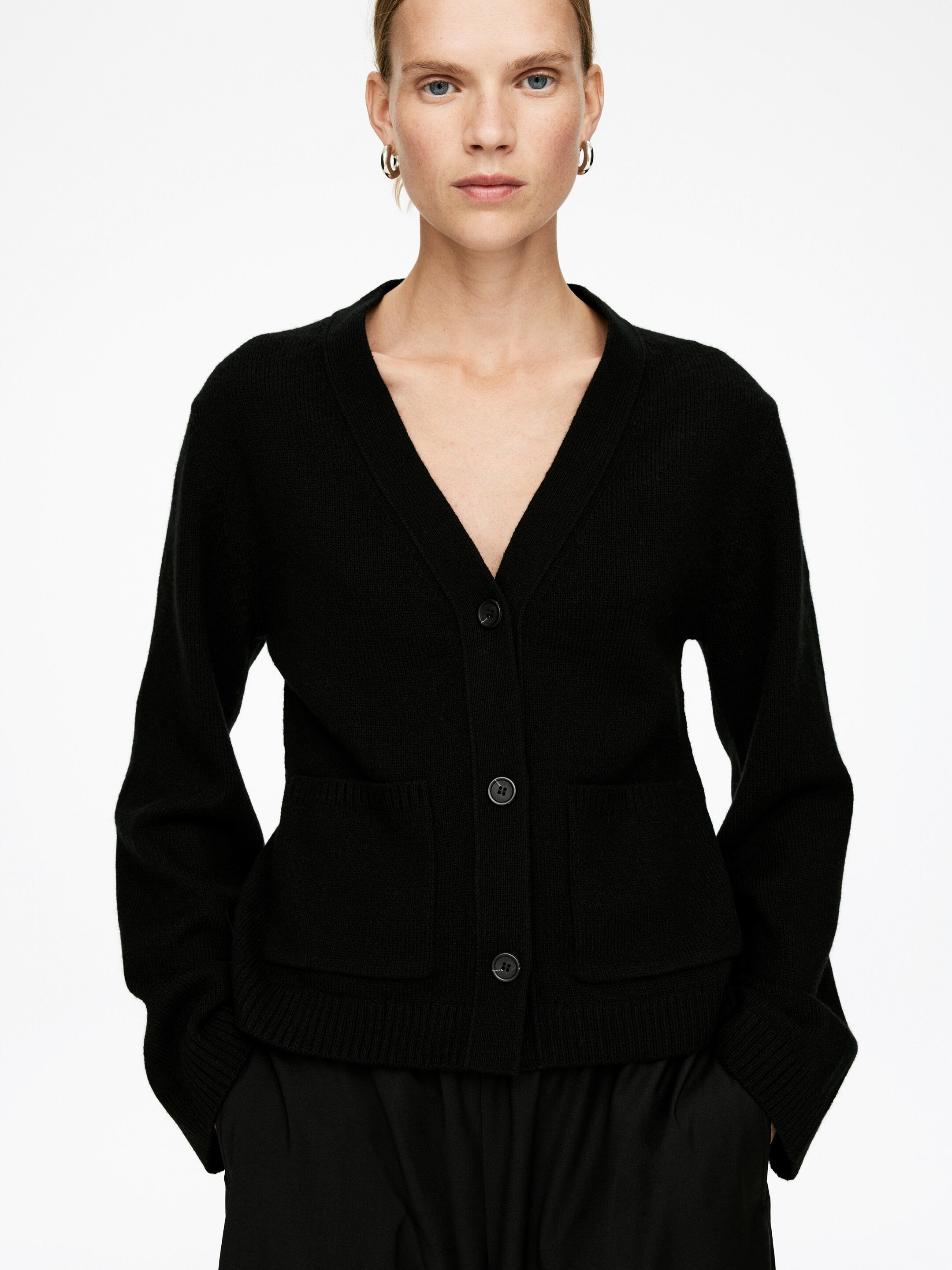 View larger image: A black knitted cardigan is being presented front-facing, featuring a V-neckline and a four-button front closure. It is designed with two patch pockets at the front and finished with ribbed cuffs and a ribbed hem.