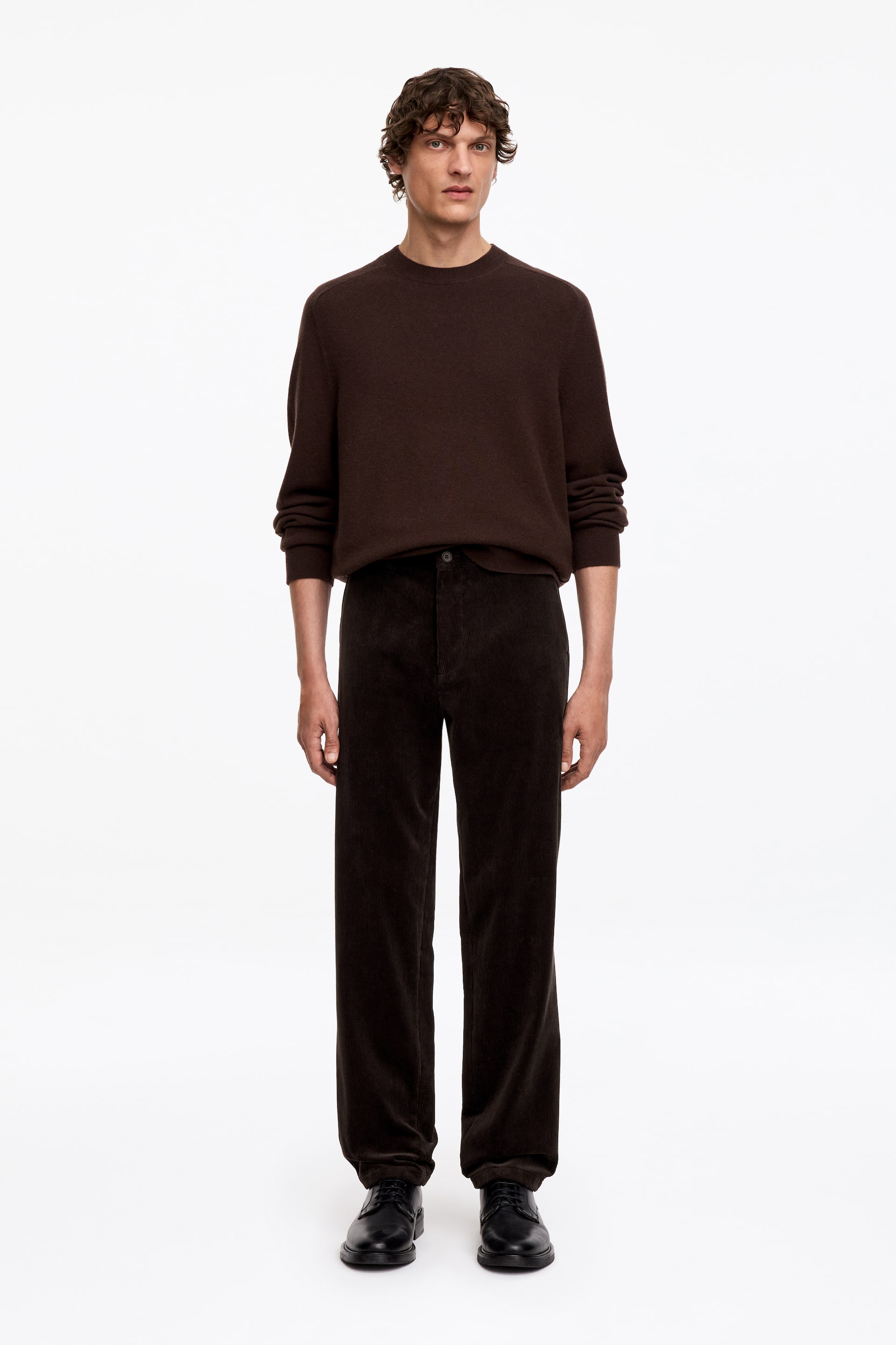 Ver imagen más grande: La modelo lleva un jersey de cuello redondo de color marrón oscuro con mangas largas, combinado con unos pantalones rectos de pana marrón oscuro y zapatos negros con cordones.