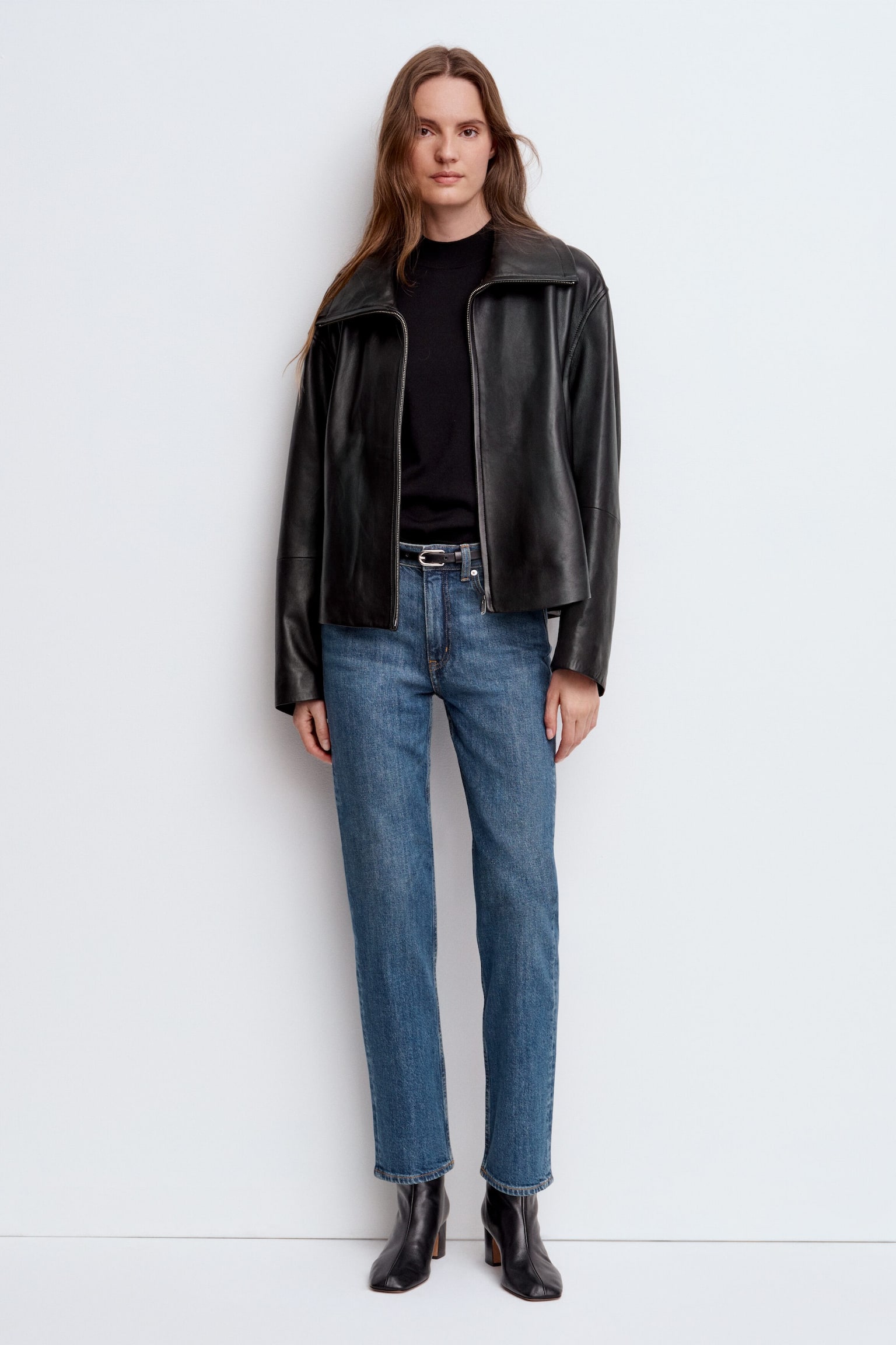 Un paio di jeans in denim blu mostra il suo DAVANTI, caratterizzato da una cintura con passanti per cintura, una chiusura con bottone e zip, e tasche frontali a cucchiaio con un taschino portamonete. I jeans presentano una gamba affusolata e corta. - 1