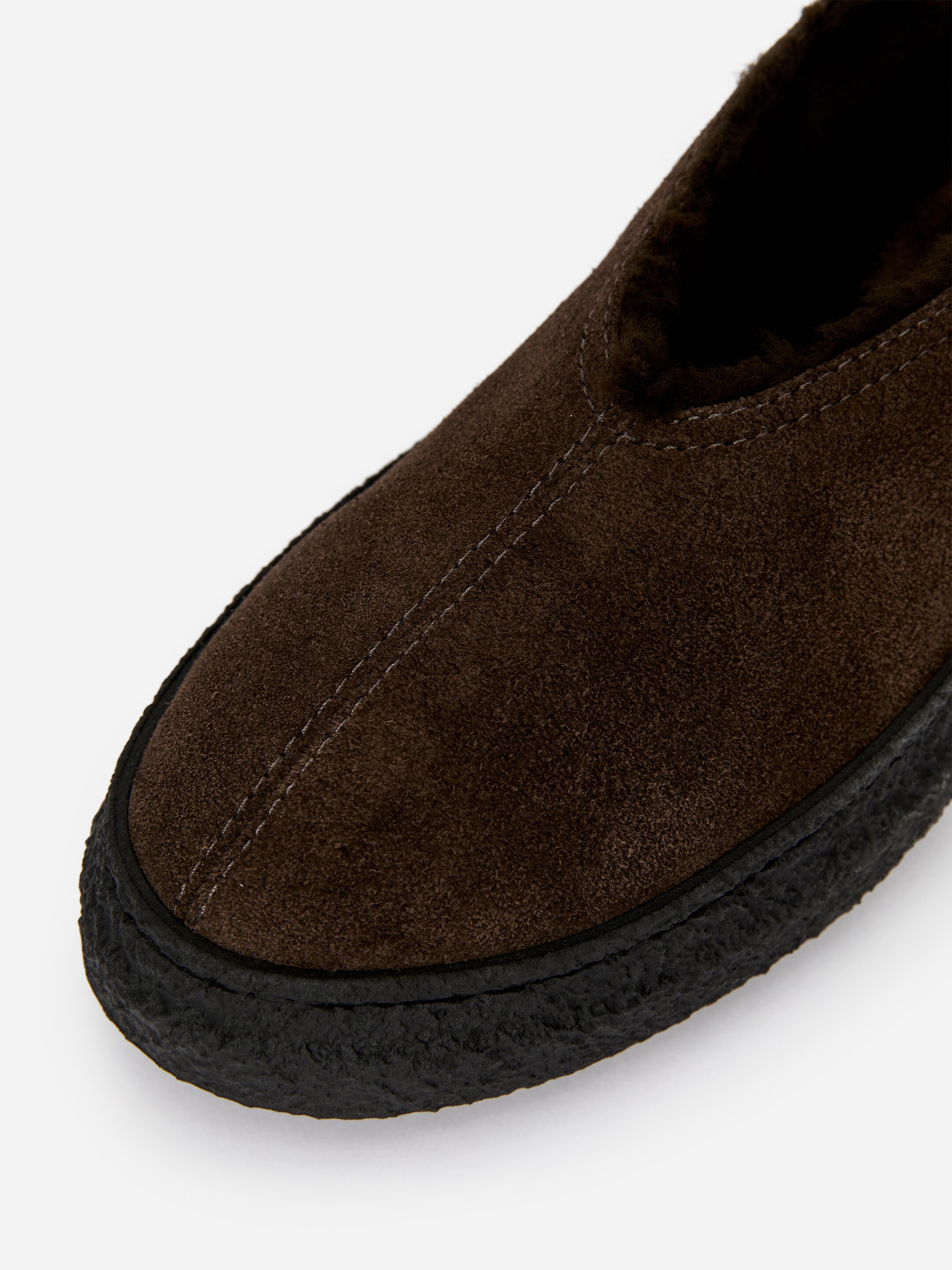 Agrandir l'image: Une pantoufle en daim marron foncé est dotée d'une épaisse semelle en crêpe noire et d'une doublure en fausse fourrure marron foncé visible autour de l'ouverture. Des coutures de couleur claire détaillent la partie supérieure du devant, descendant le long du centre.