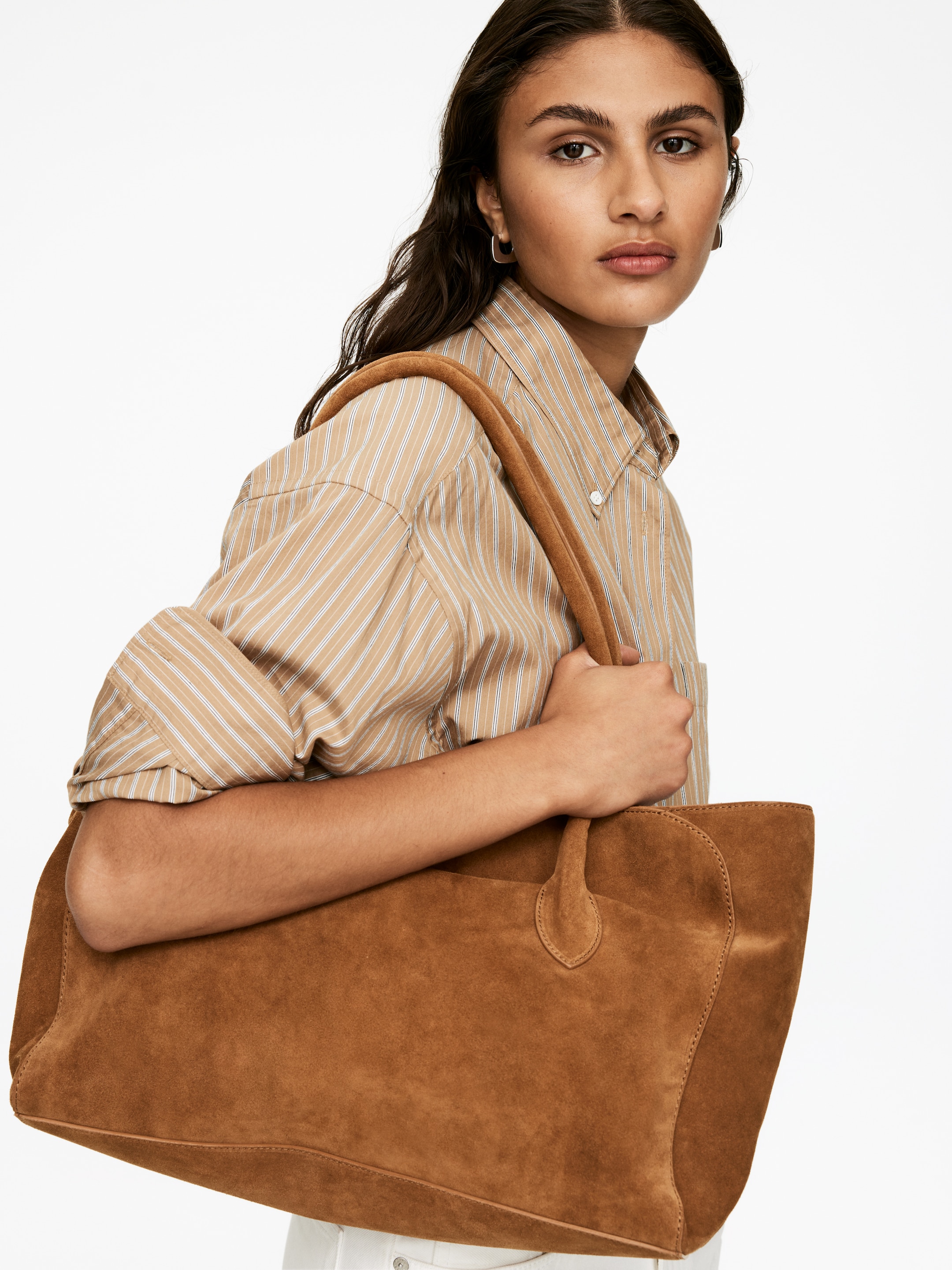 Visualizza immagine più grande: Una borsa tote in morbida pelle scamosciata marrone caldo viene portata, mettendo in mostra la sua texture soffice, i pannelli laterali strutturati con cuciture prominenti e due manici superiori che si alzano dalla parte superiore aperta.