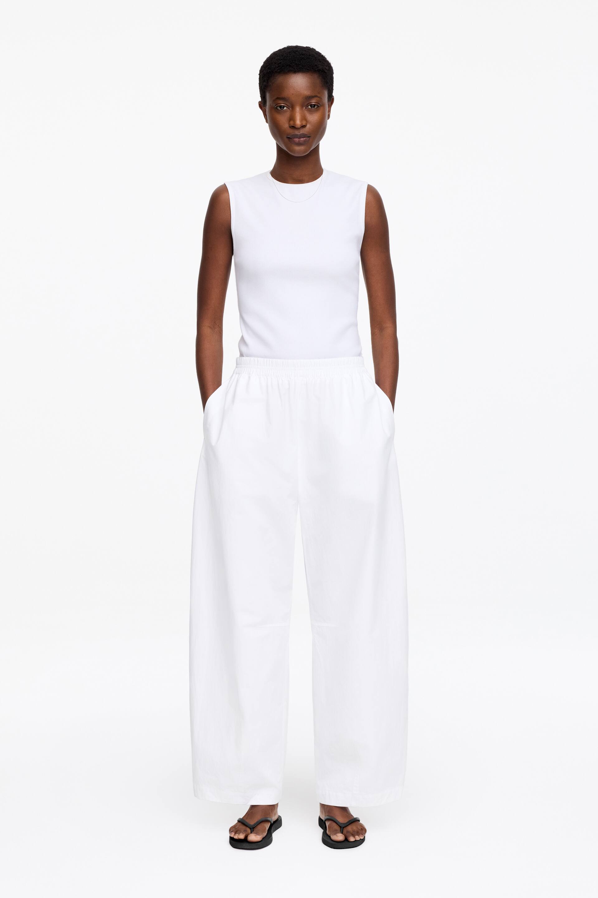Zobrazit větší obrázek: Bílý top bez rukávů s kulatým výstřihem a přiléhavým střihem, zatímco bílé kalhoty s širokými nohavicemi mají elastický pas a boční kapsy.