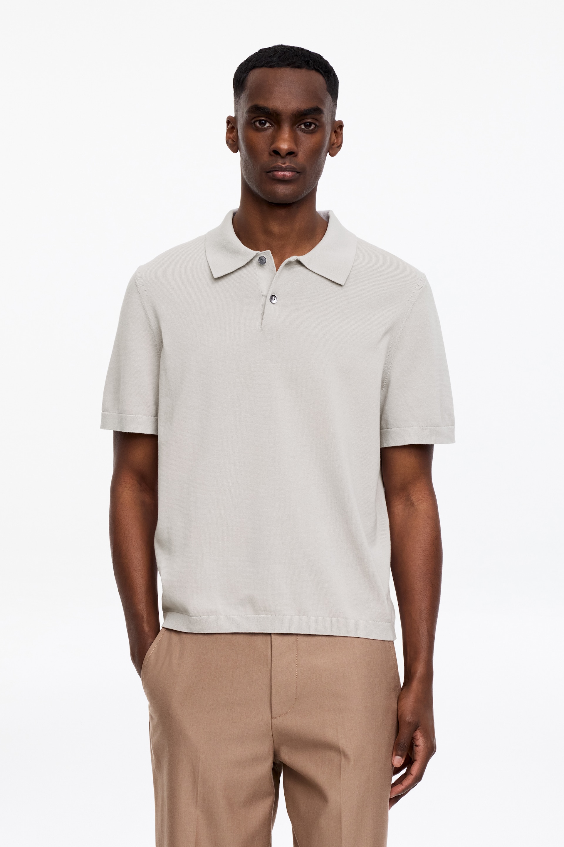 Zobrazit větší obrázek: Světle šedé pletené polo tričko s klasickým límečkem, dvouknoflíkovou légou s tmavými knoflíky, krátkými rukávy s dokončenými manžetami a rovným lemem.