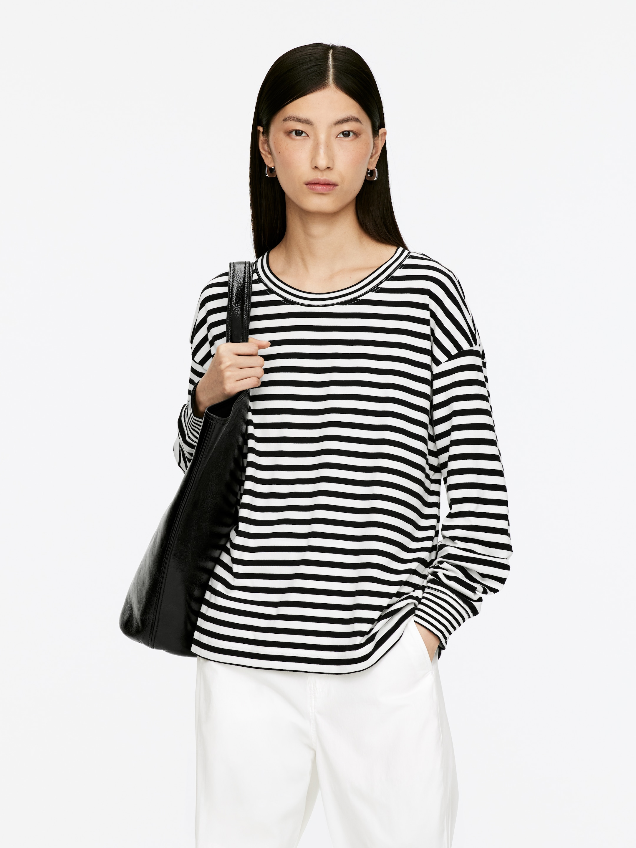 View larger image: A black and white striped long-sleeved top with a relaxed fit, featuring a crew neck and ribbed cuffs, is being presented from the front, styled with white pants and a black bag draped over the left shoulder.
