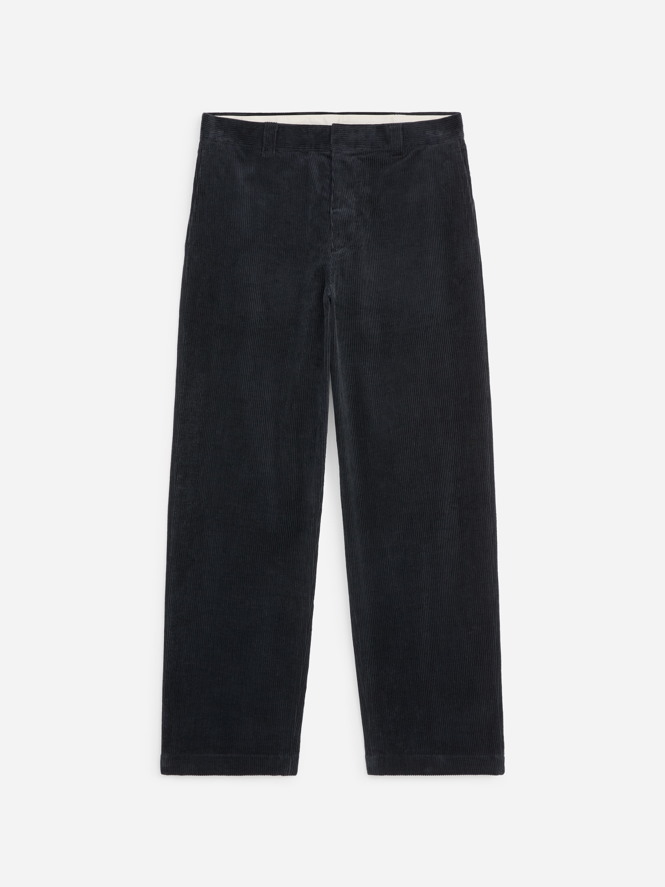 La modella indossa pantaloni neri in velluto a coste a gamba larga, in piedi con le mani inserite nelle tasche laterali. I pantaloni sono abbinati a una camicia azzurra con bottoni lasciata fuori e a scarpe nere.