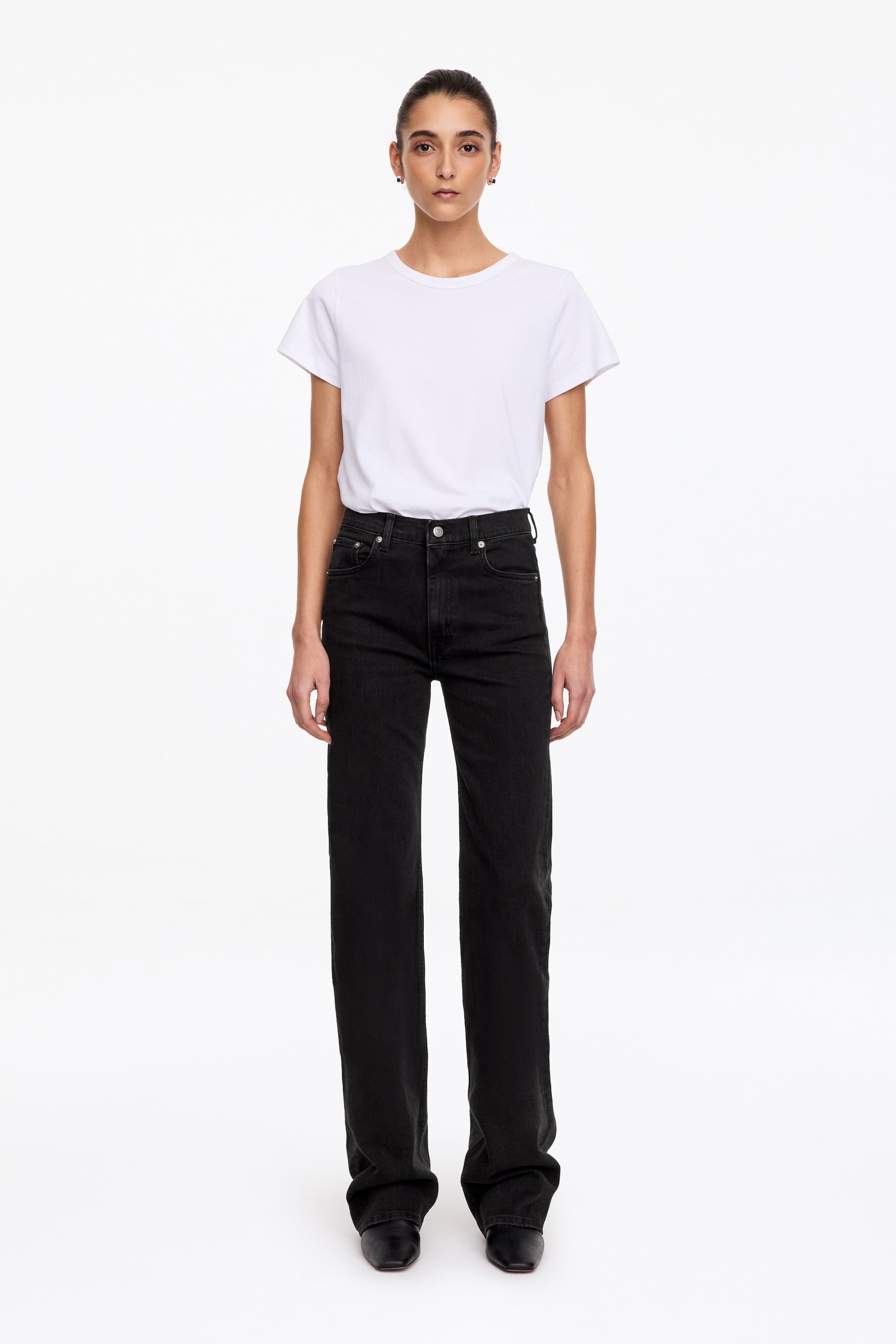 Visualizza immagine più grande: Jeans bootcut neri a vita alta e vestibilità slim indossati dalla modella, abbinati a una T-shirt bianca infilata nei pantaloni e scarpe nere. I jeans presentano un classico design a cinque tasche e una gamba che cade leggermente sul bordo delle calzature.