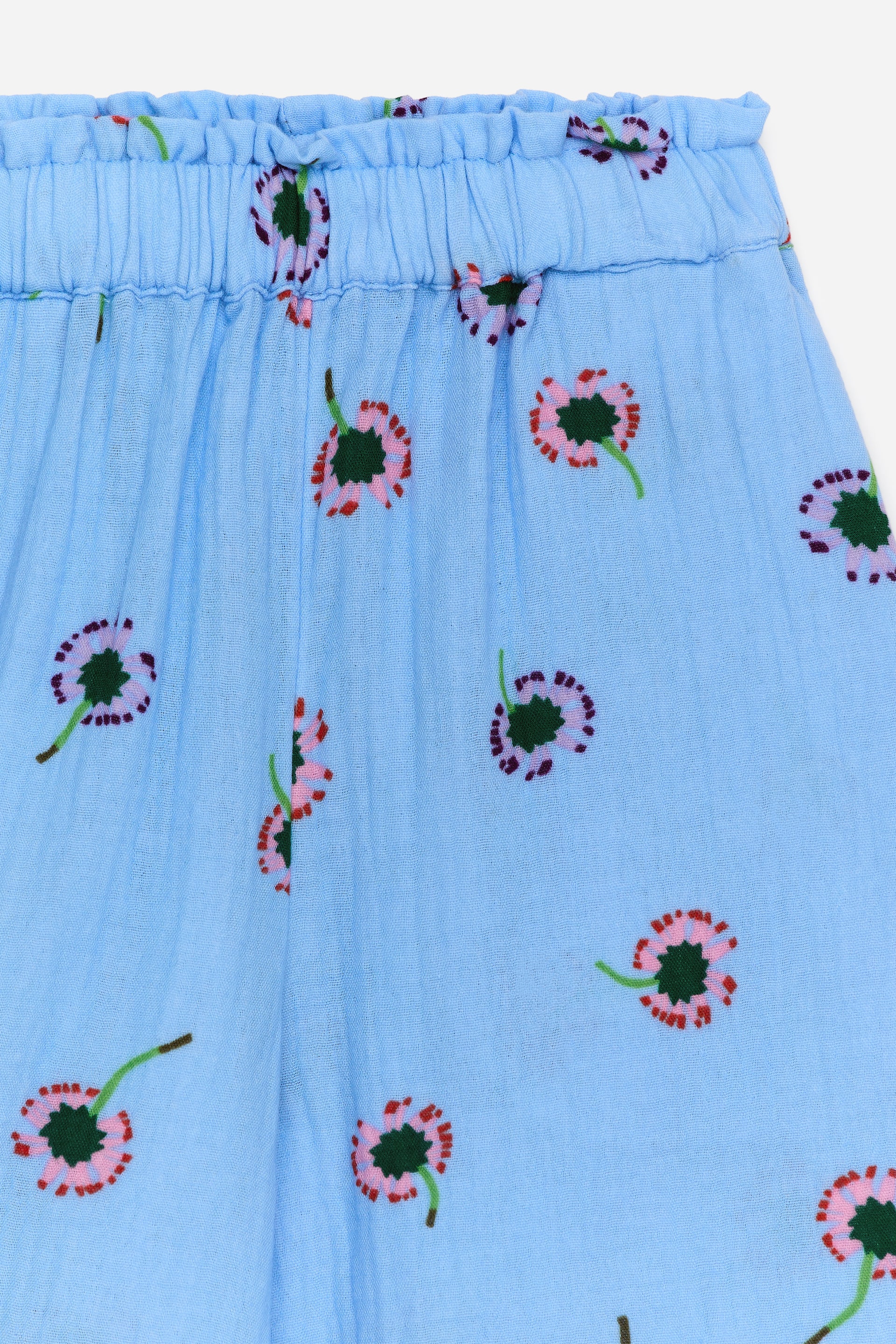 Größeres Bild ansehen: Ein hellblaues Kleidungsstück aus geknittertem Stoff verfügt über einen elastischen, gerafften Bund. Das Kleidungsstück zeigt ein sich wiederholendes Muster stilisierter Blumen, jede mit einem dunkelgrünen Zentrum und rosa Blütenblättern mit roten Umrissen.