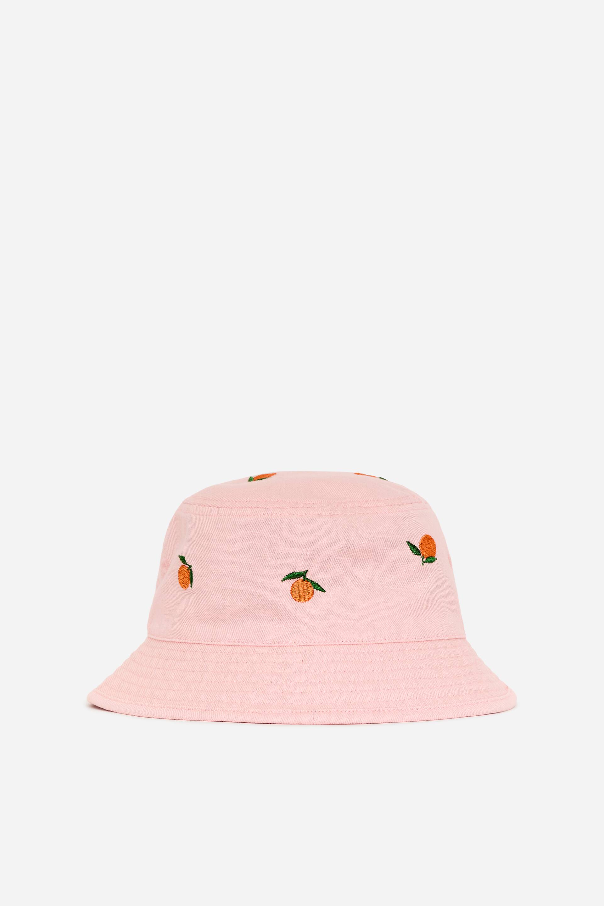 Visa större bild: En rosa denimhatt med broderade orange fruktdetaljer över hela och en medellång brätte.