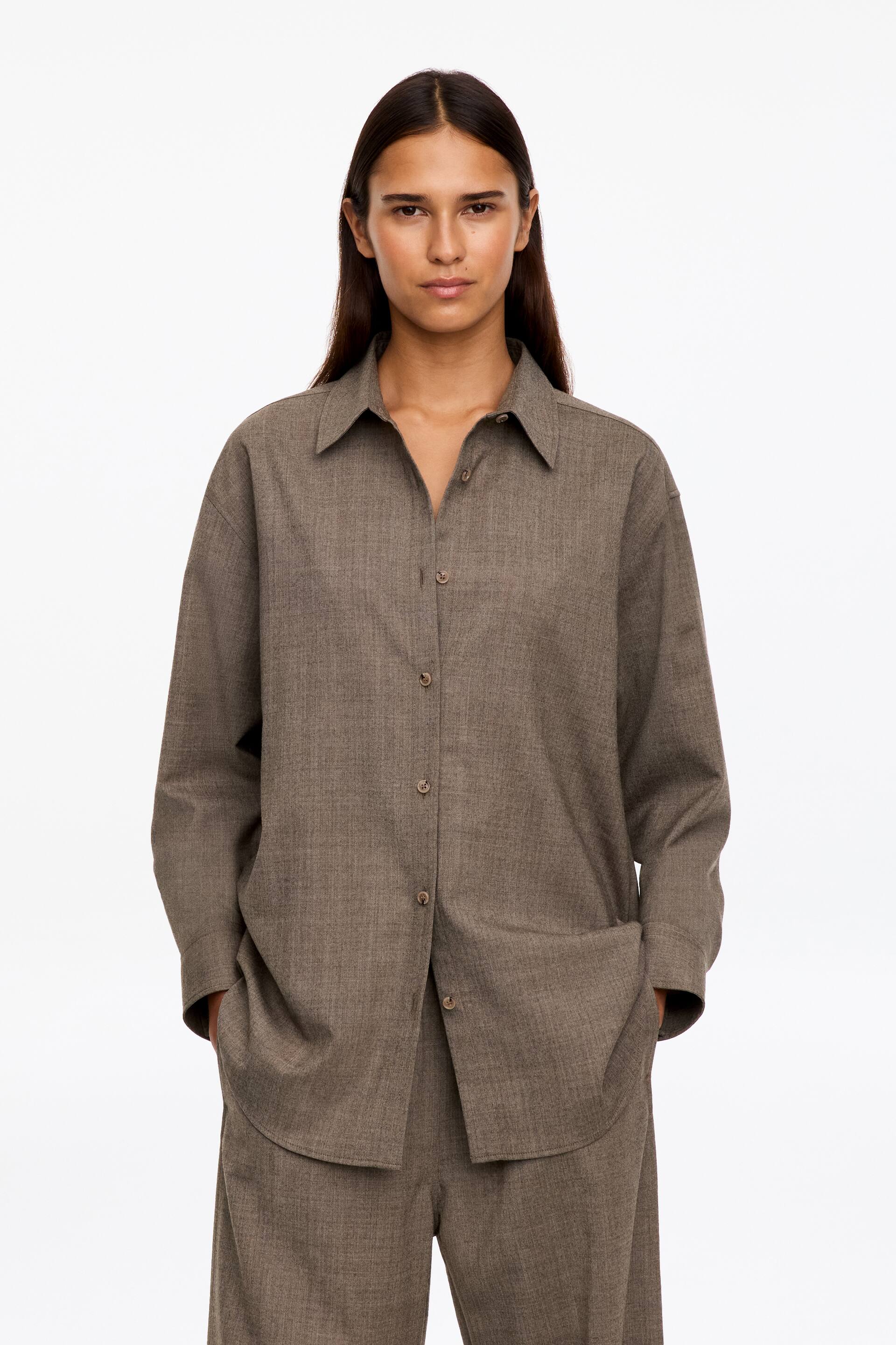 Ver imagen más grande: La modelo lleva una camisa marrón de corte relajado, con botones delanteros, confeccionada en franela de mezcla de lana. La camisa presenta un cuello clásico, un bajo curvado y mangas largas, y se combina con un pantalón a juego.