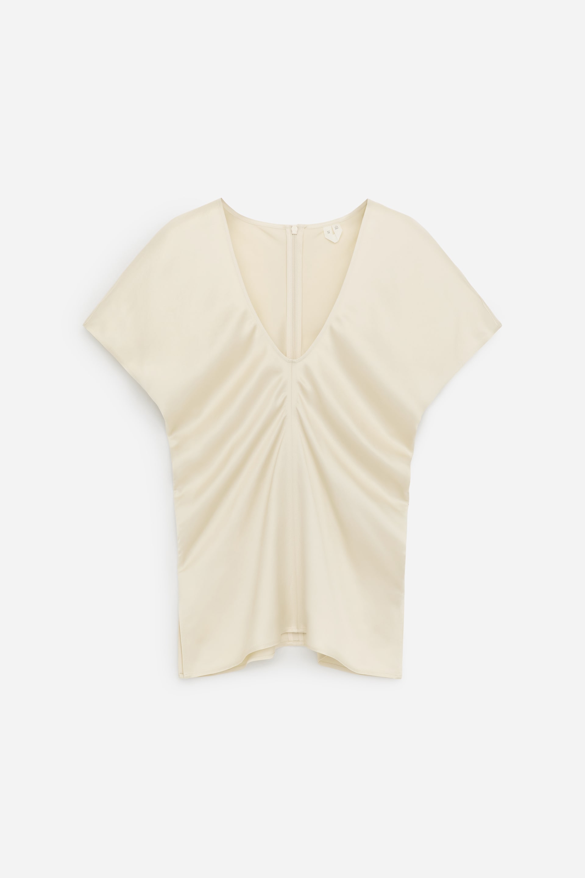 Agrandir l'image: Un haut en satin de couleur crème est présenté de face, avec un profond décolleté en V et des manches dolman courtes et amples. Des fronces créent un effet drapé au centre avant, et une fermeture éclair courte est visible à l'arrière du cou.