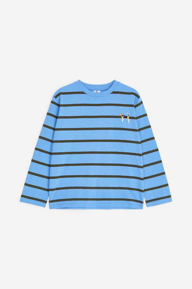 Een lichtblauw T-shirt met lange mouwen is van voren te zien, met horizontale donkergroene strepen en een kleine geborduurde hond op de linkerbovenborst. - 1