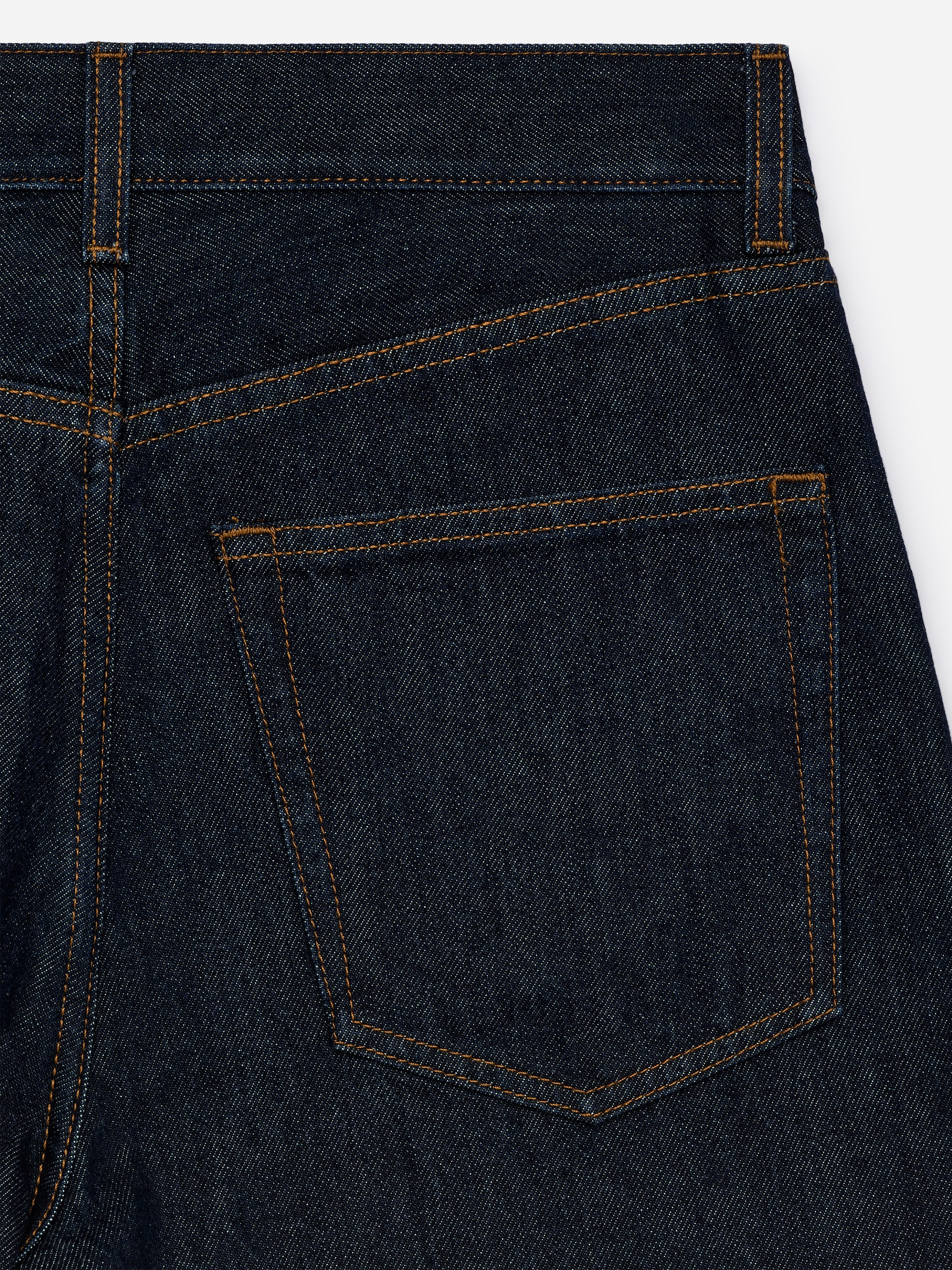 Agrandir l'image: Un jean en denim à lavage foncé présente son dos, révélant une poche arrière unique détaillée avec des coutures orange contrastantes. Une ceinture, un empiècement courbé et un passant de ceinture sont également visibles.